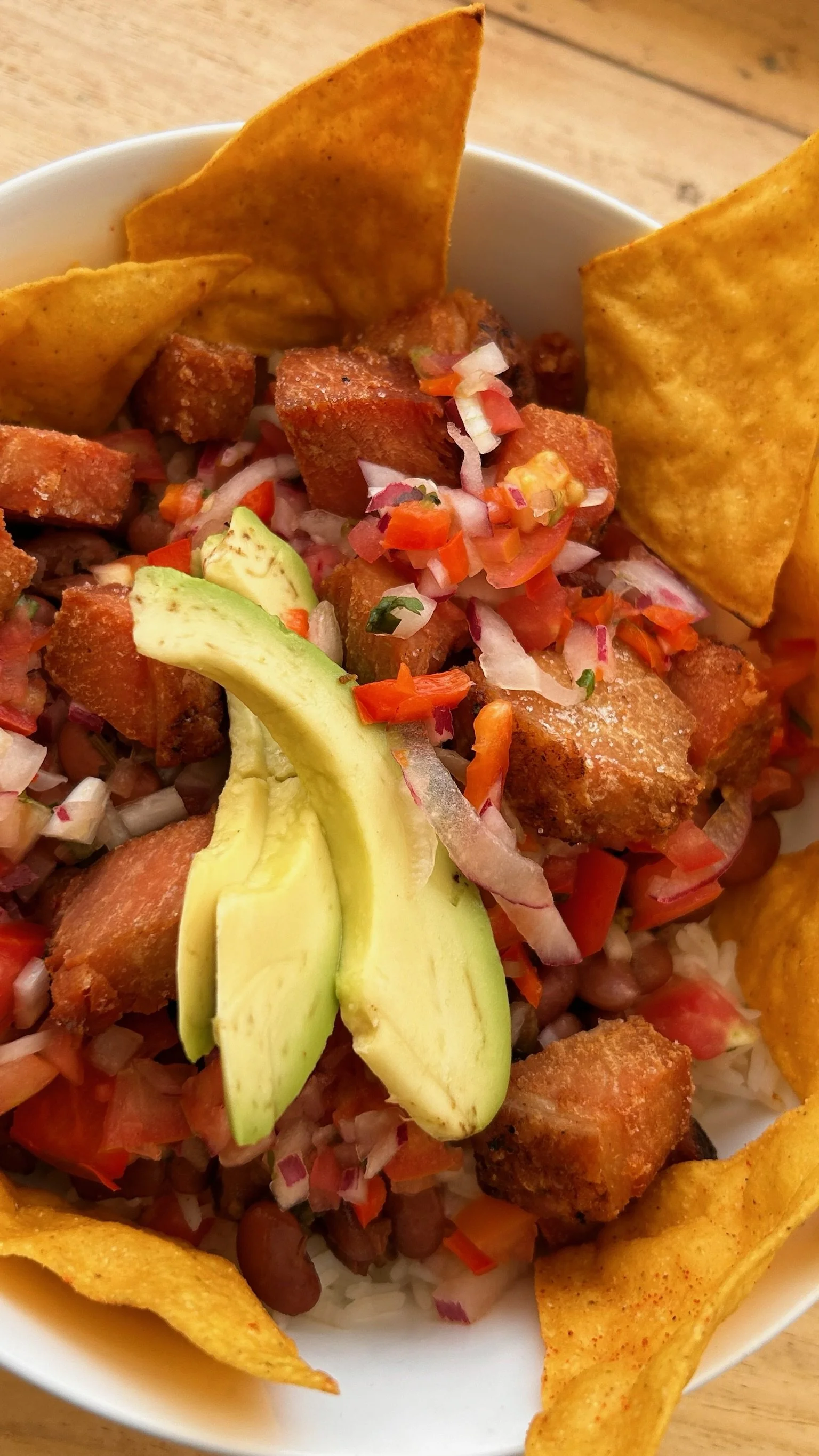 Tacos filled with fried chicken, diced tomatoes, chopped onions, sliced avocado, and tortilla chips