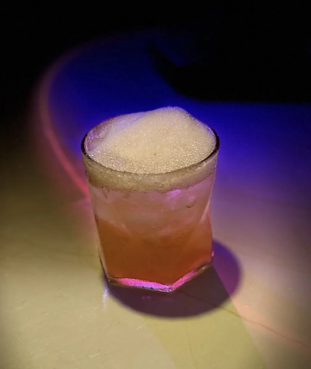 A pisco sour cocktail, illuminated by colorful lighting creating a vibrant ambiance.