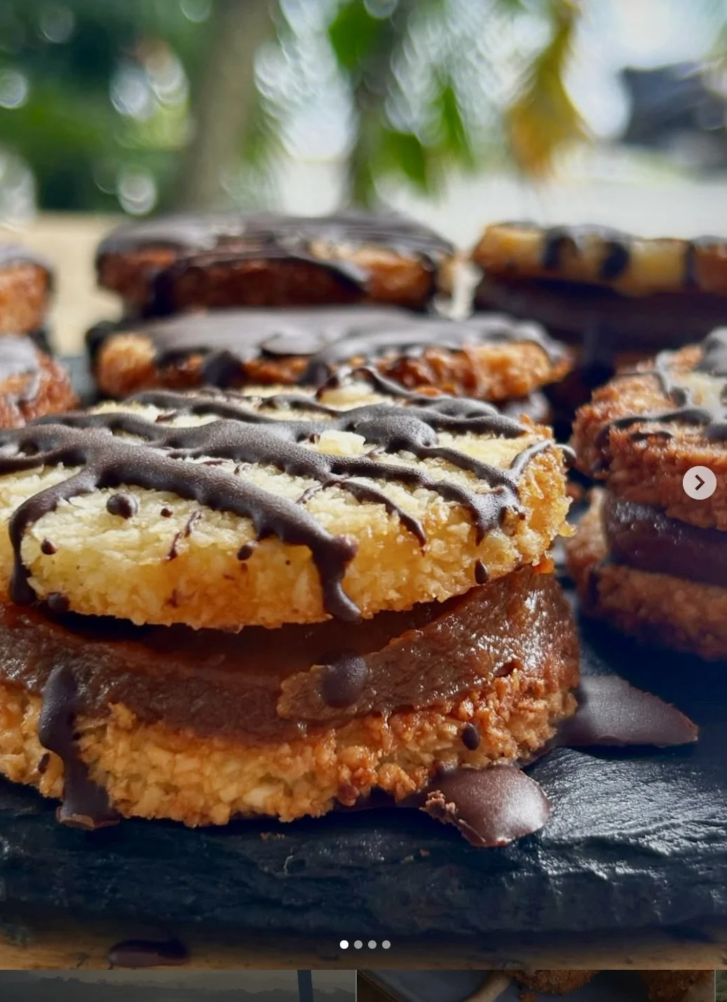 Close-up of gluten free coconut alfajores topped with chocolate drizzle on a black surface.