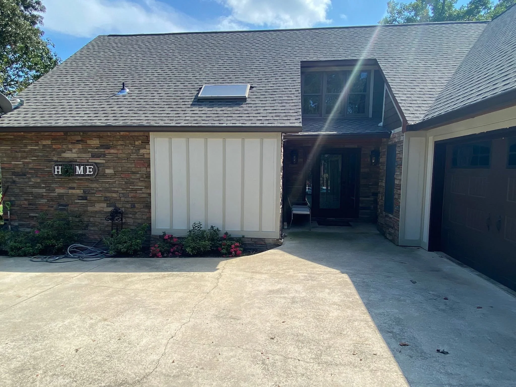 The image shows the front yard of a house with James Hardie siding, a concrete driveway, a section of landscaping, and a stone and wood house with a gabled roof, skylight window, and custom french double doors. 