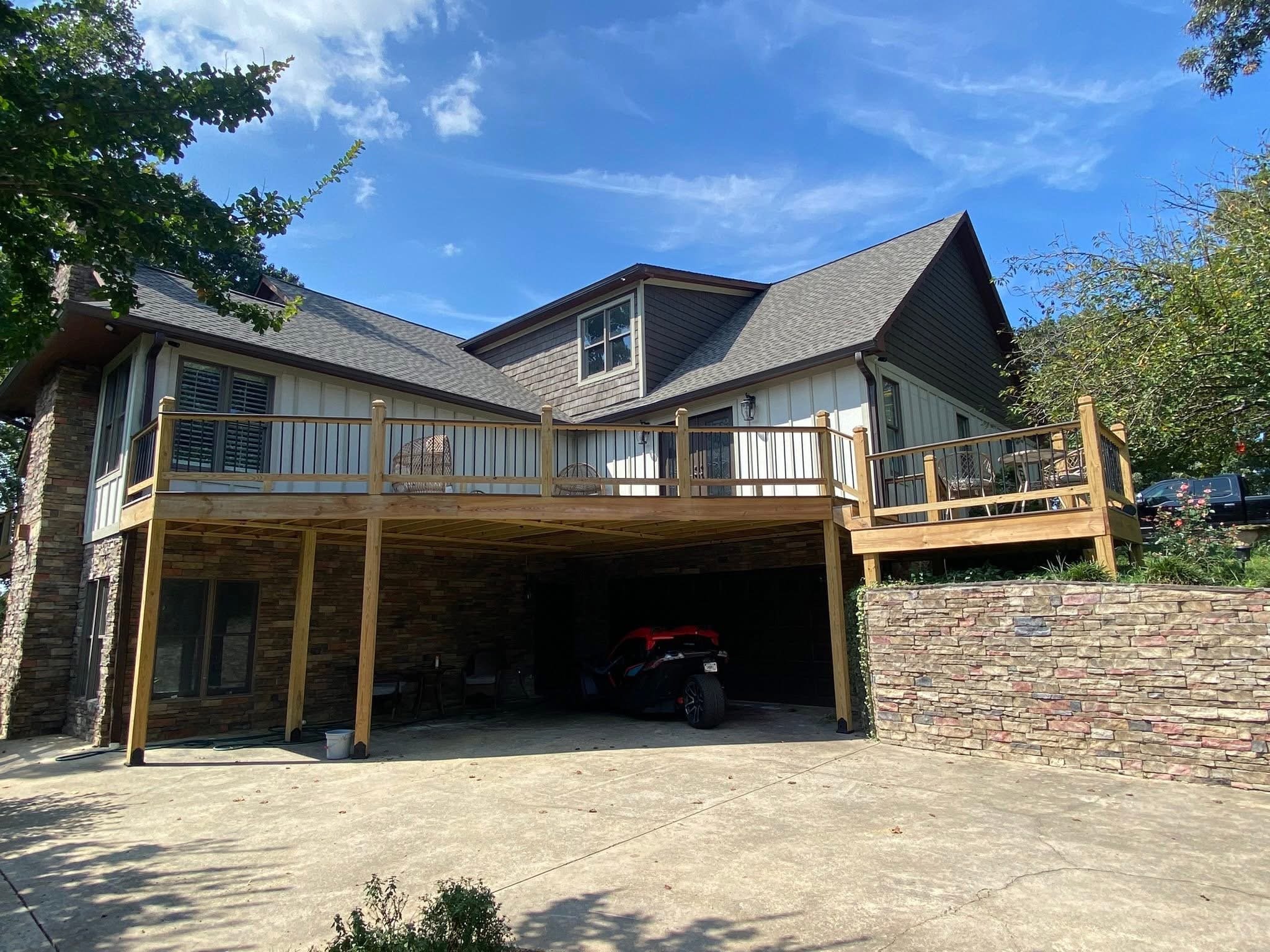 A two-story house with a partially enclosed upper deck including trex decking, a gabled roof with dark shingles, and a back yard with a tree and a clear blue sky.