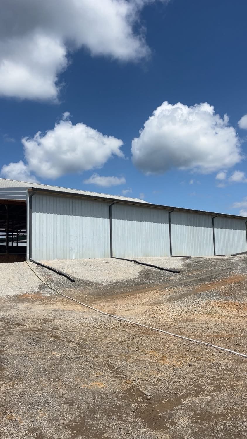 Metal building on a gravel surface under a blue sky with white clouds.