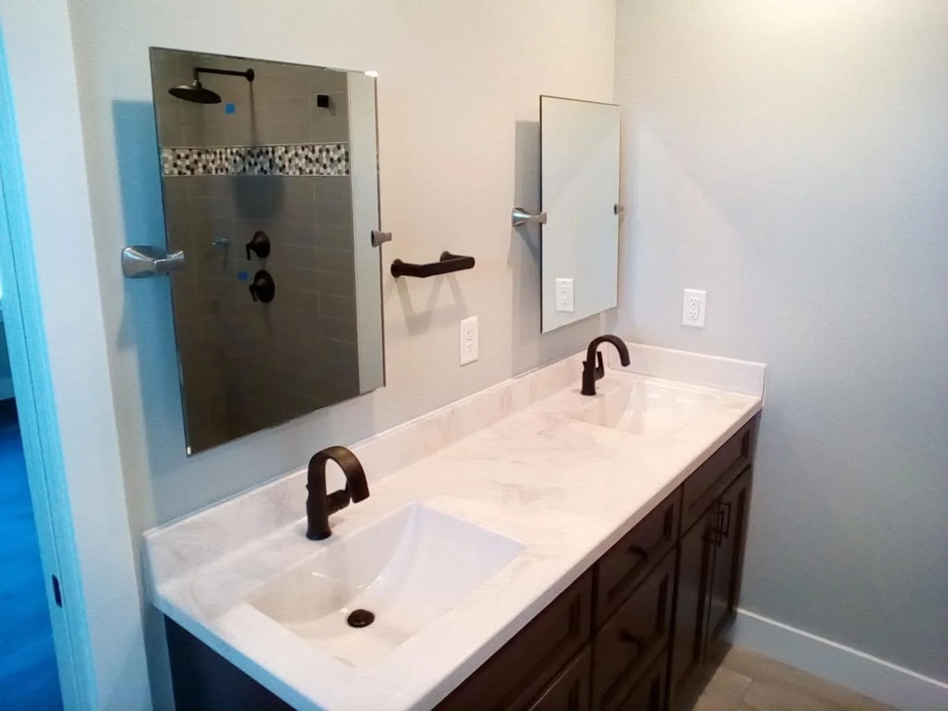 Bathroom vanity with double sinks, dark faucets, large mirror, and a separate shower area with a tiled wall.