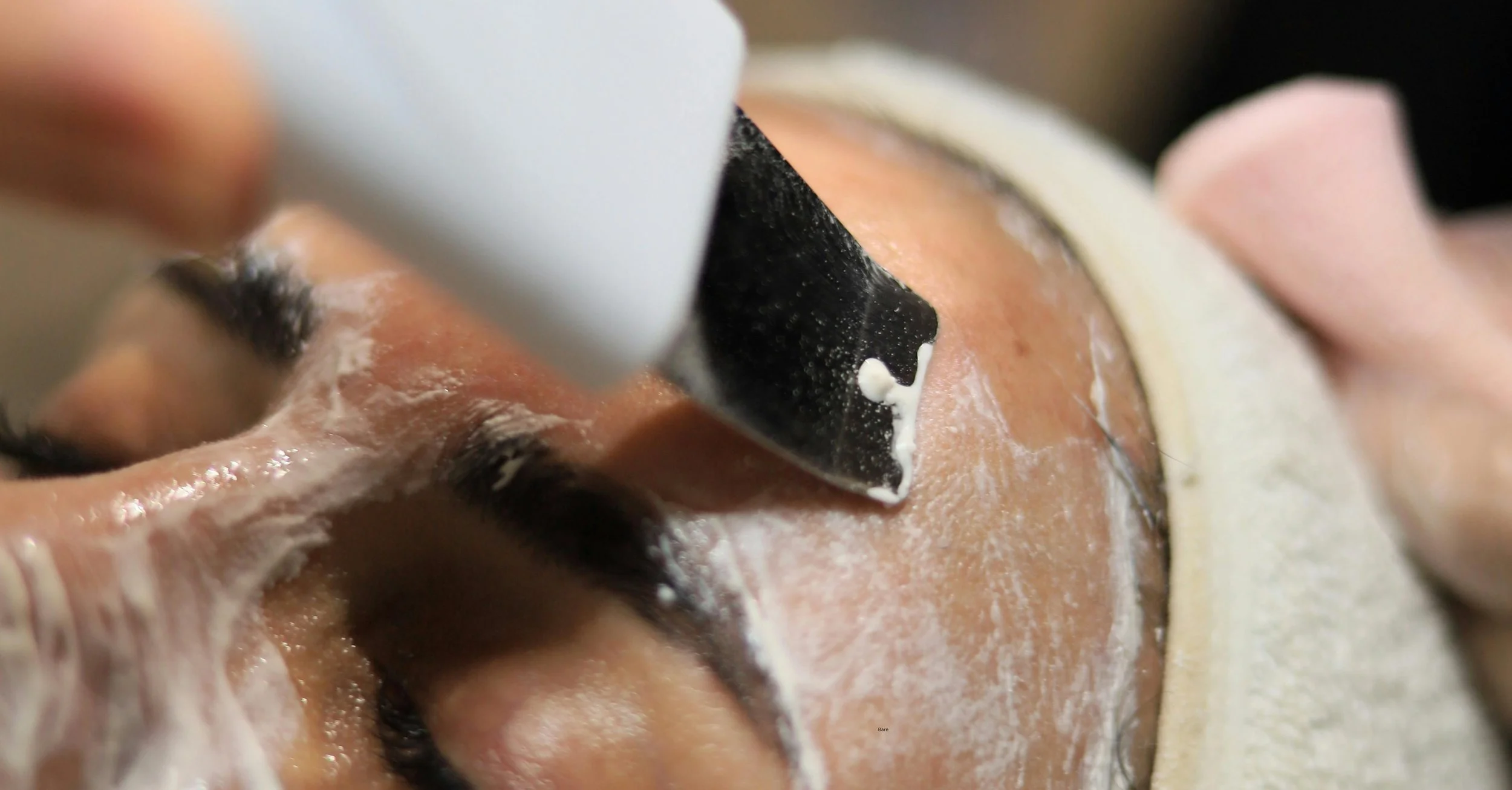 Close-up of a person receiving a facial treatment with a black facial mask being applied to their face.