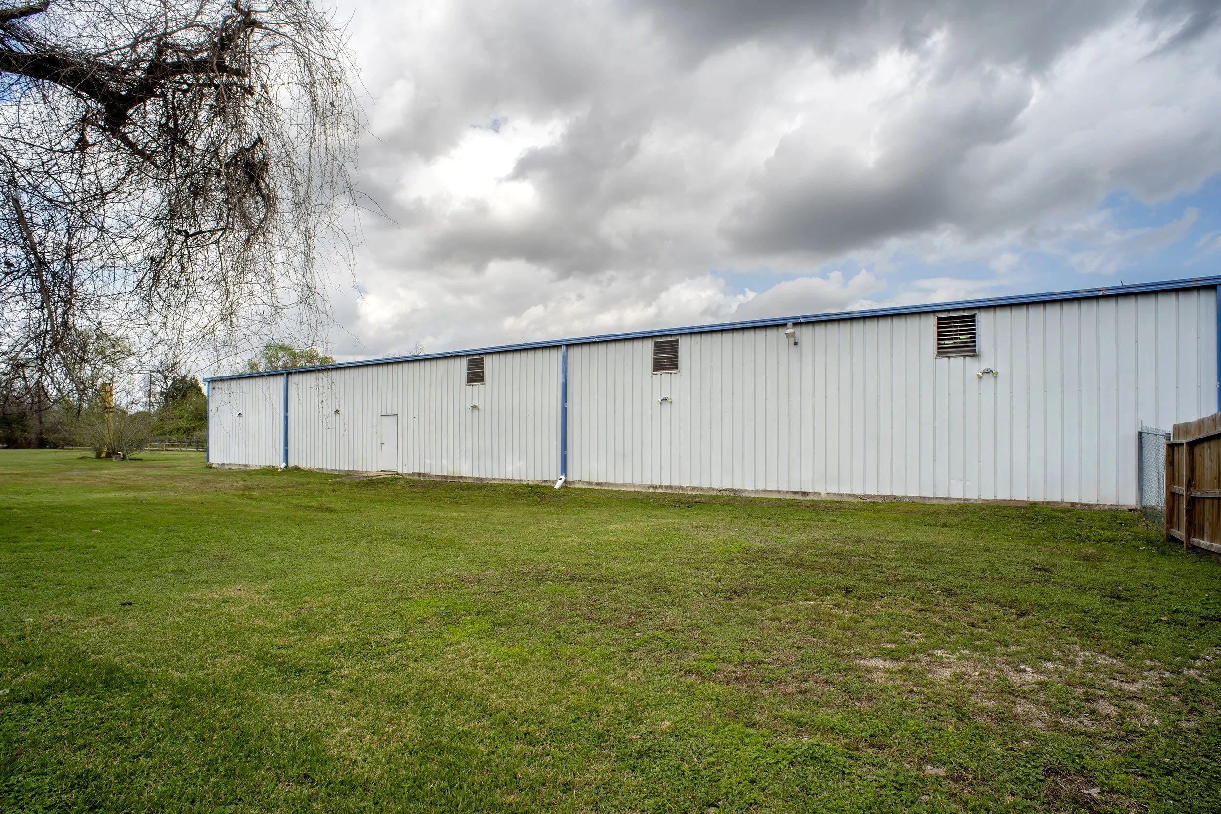 A large white building with blue trim on a grassy lawn, with ventilation vents on the side and a cloudy sky overhead.