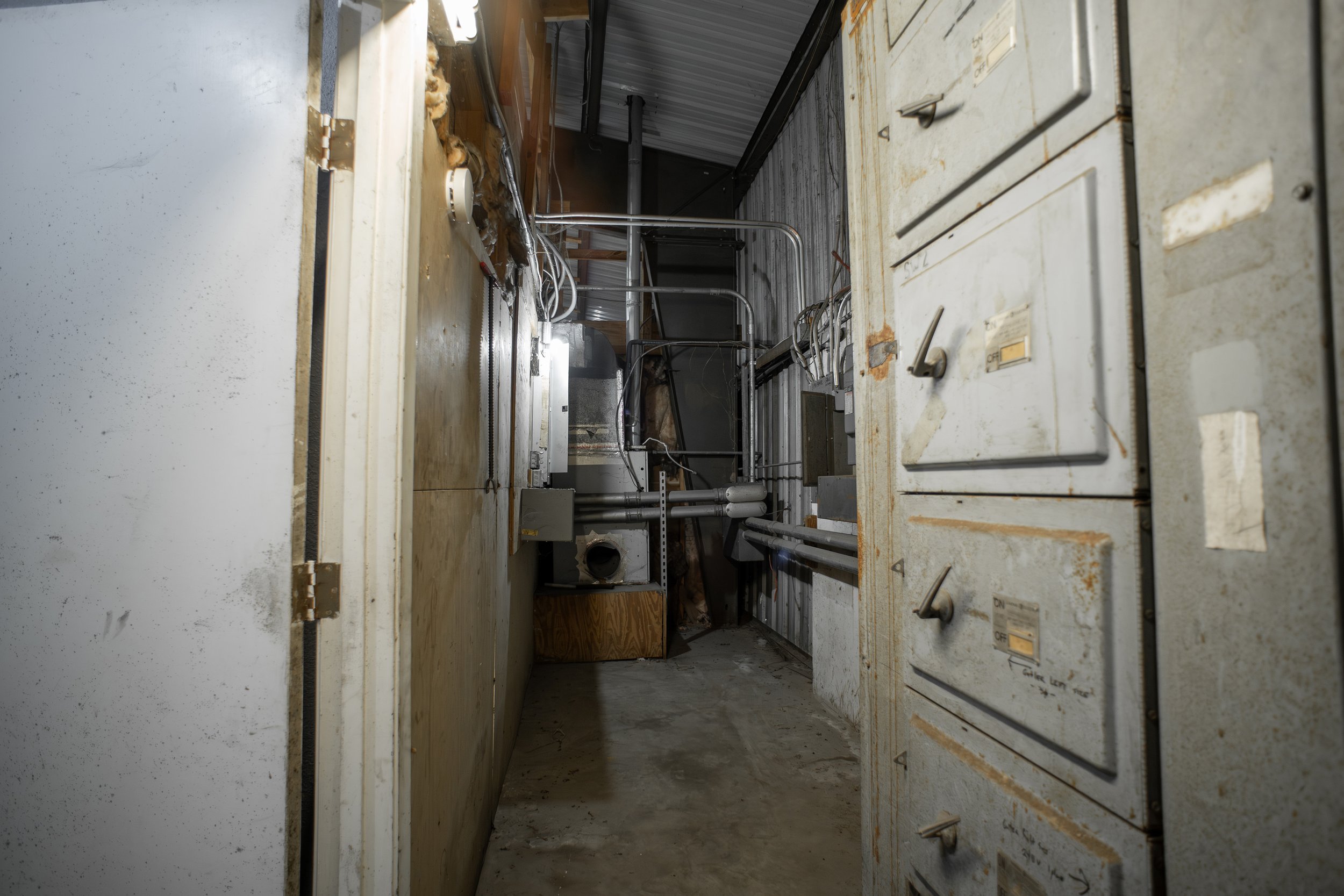 View inside an industrial or commercial space with metal pipes, electrical wiring, and a metal cabinet or control panel.