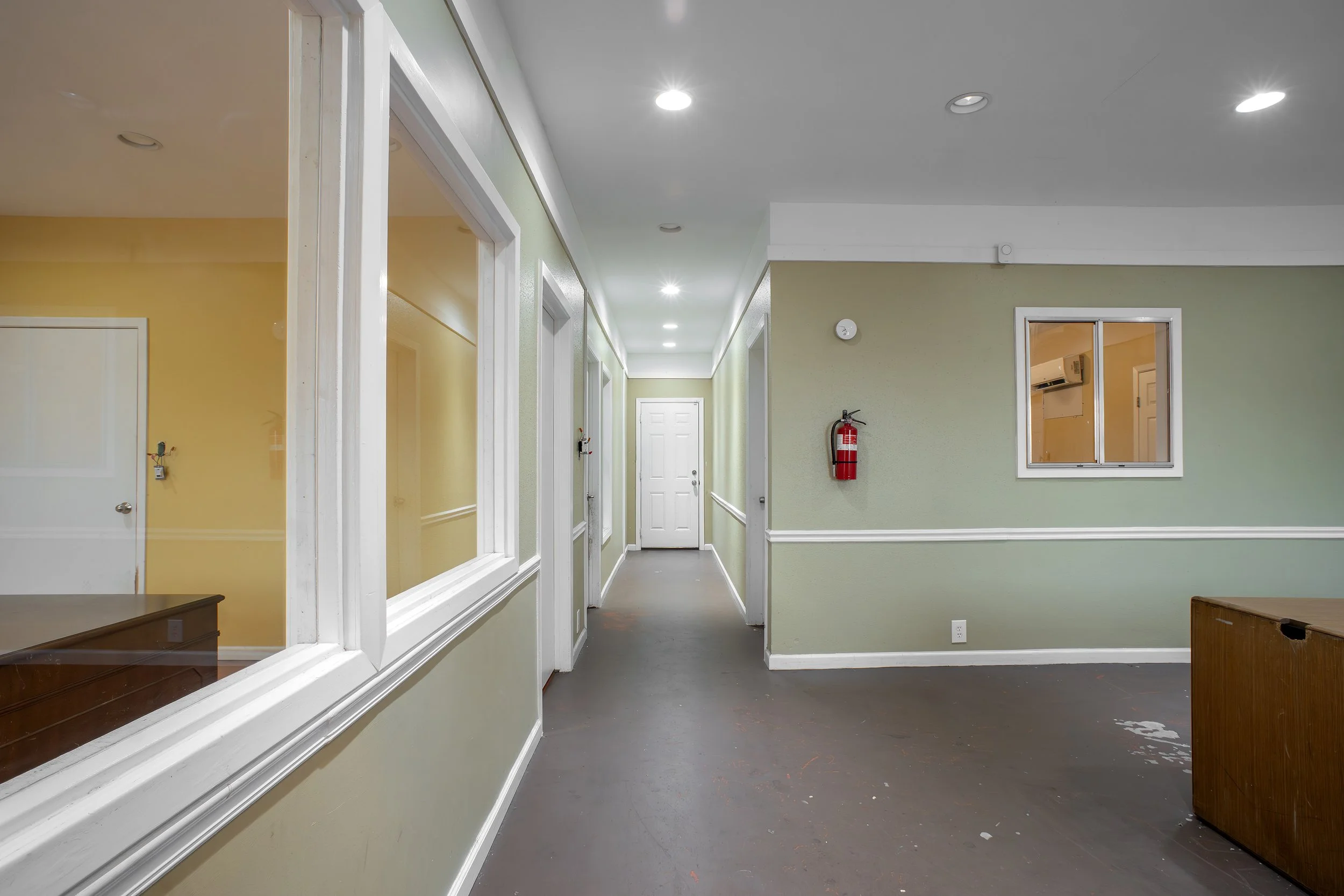 Interior of a hallway with white doors, green and yellow walls, a fire extinguisher, and ceiling lights.