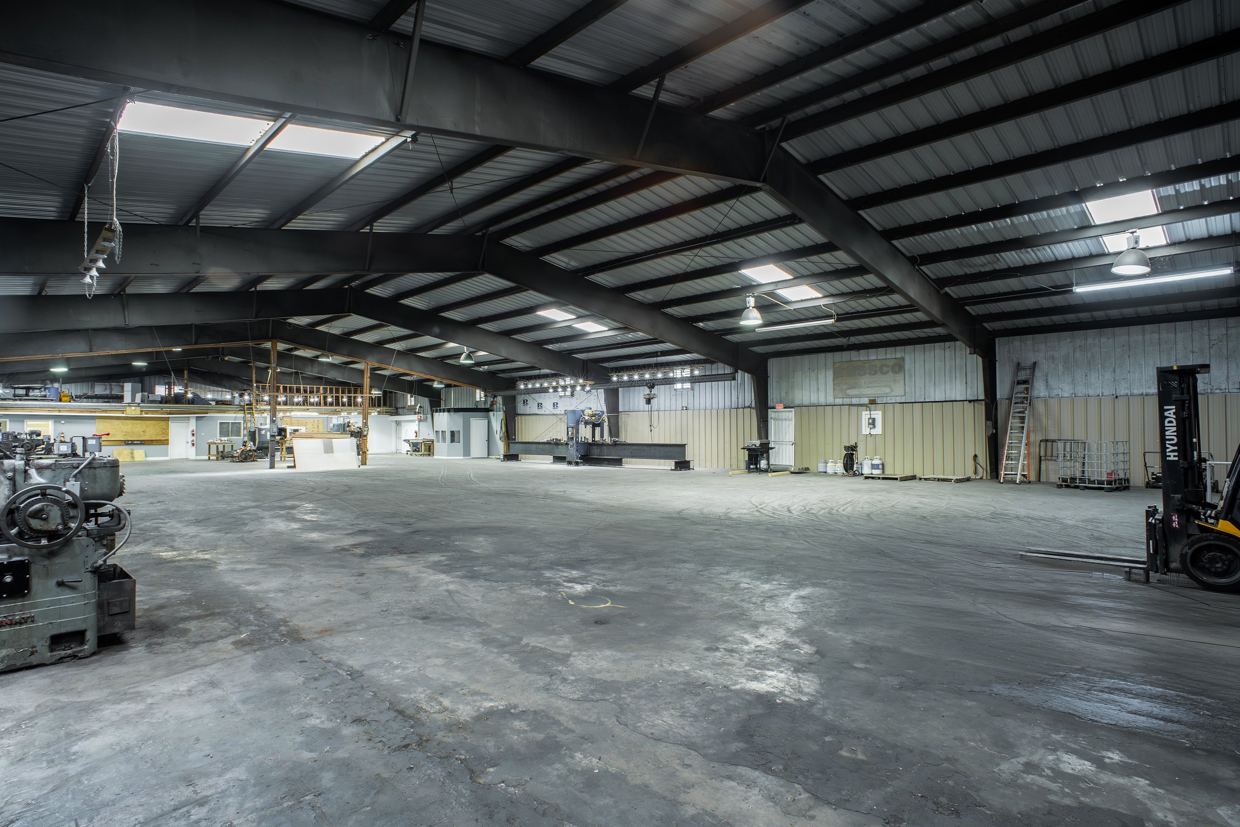 Interior of a large industrial warehouse with metal walls and ceiling, scattered equipment, and workbenches.