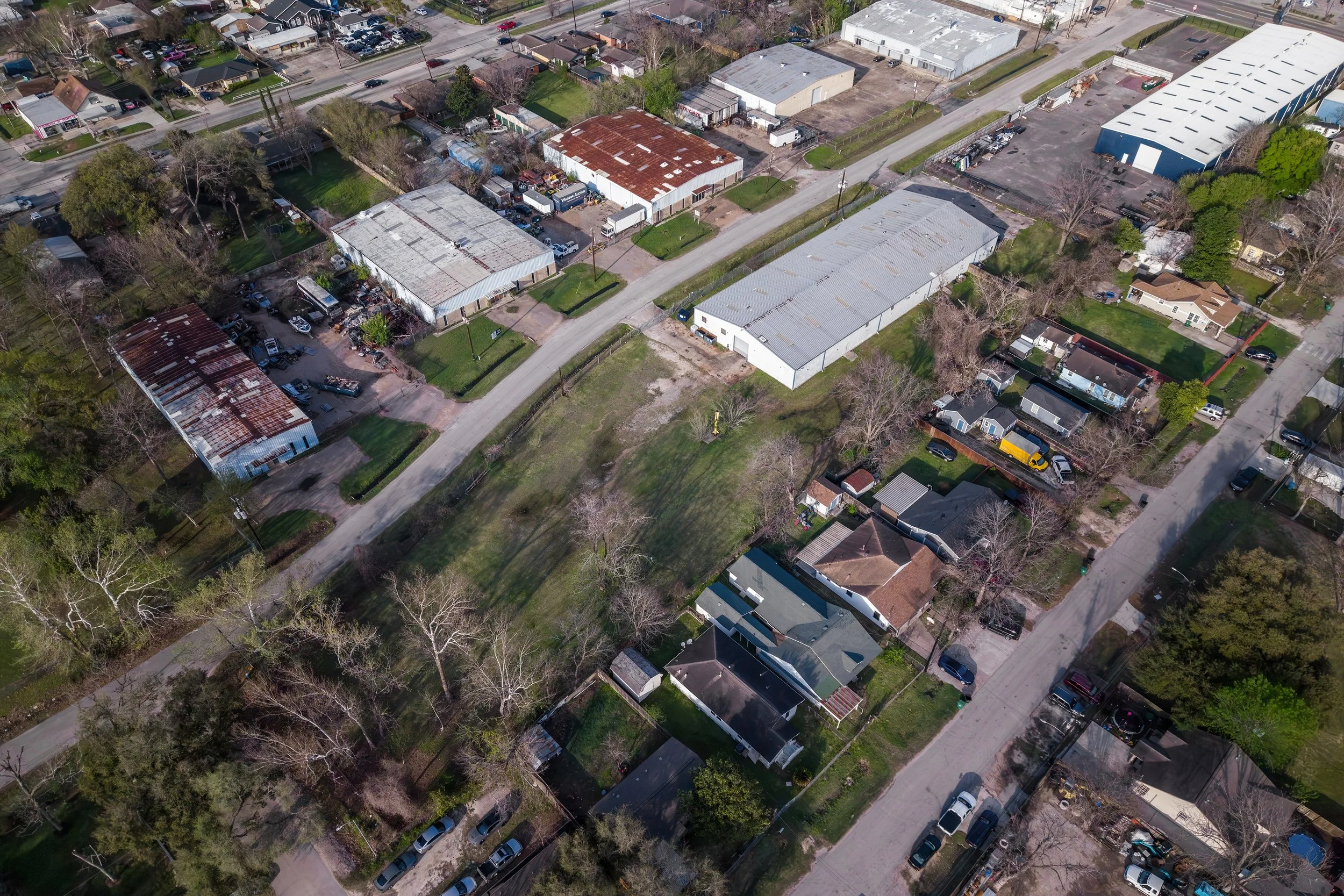 An aerial view of a mixed residential and industrial area with houses, trees, and large warehouse buildings.