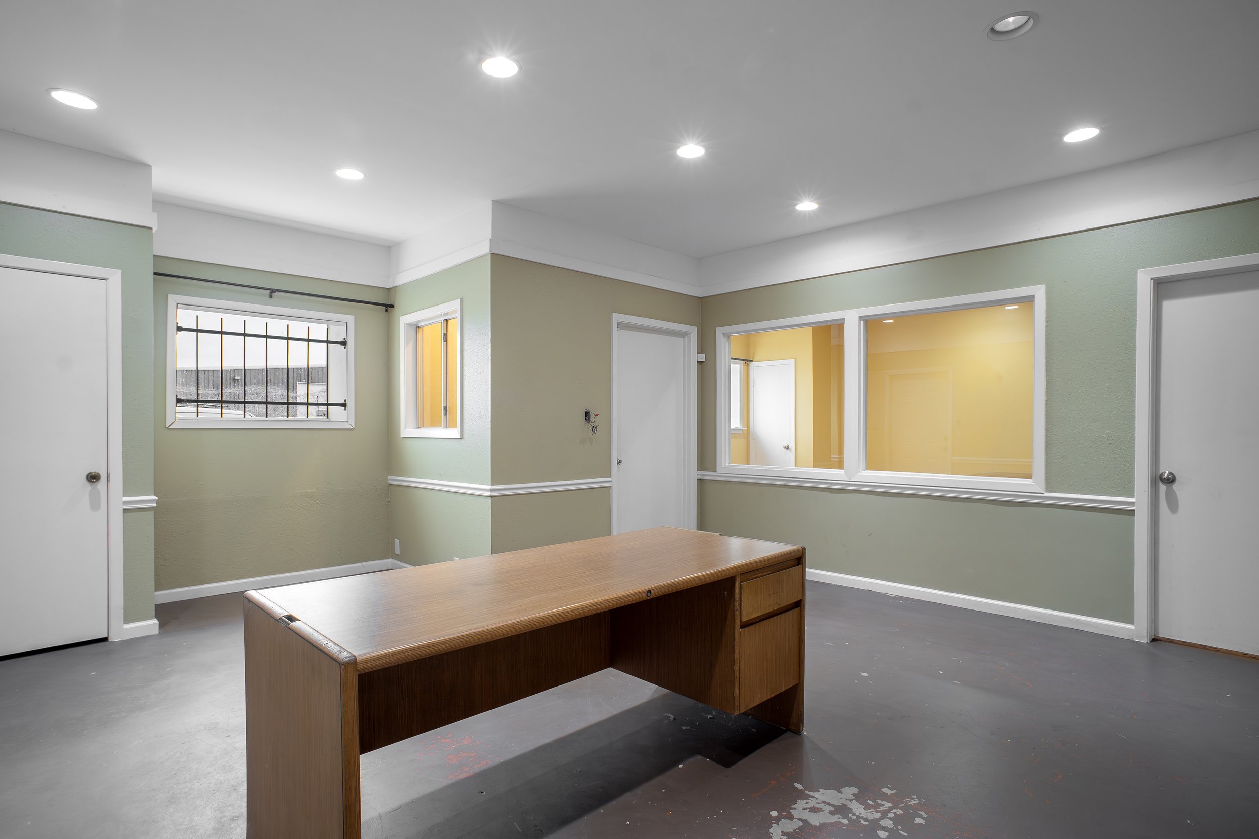 An empty room with green walls, white trim, a wooden table, and multiple windows, some with bars.