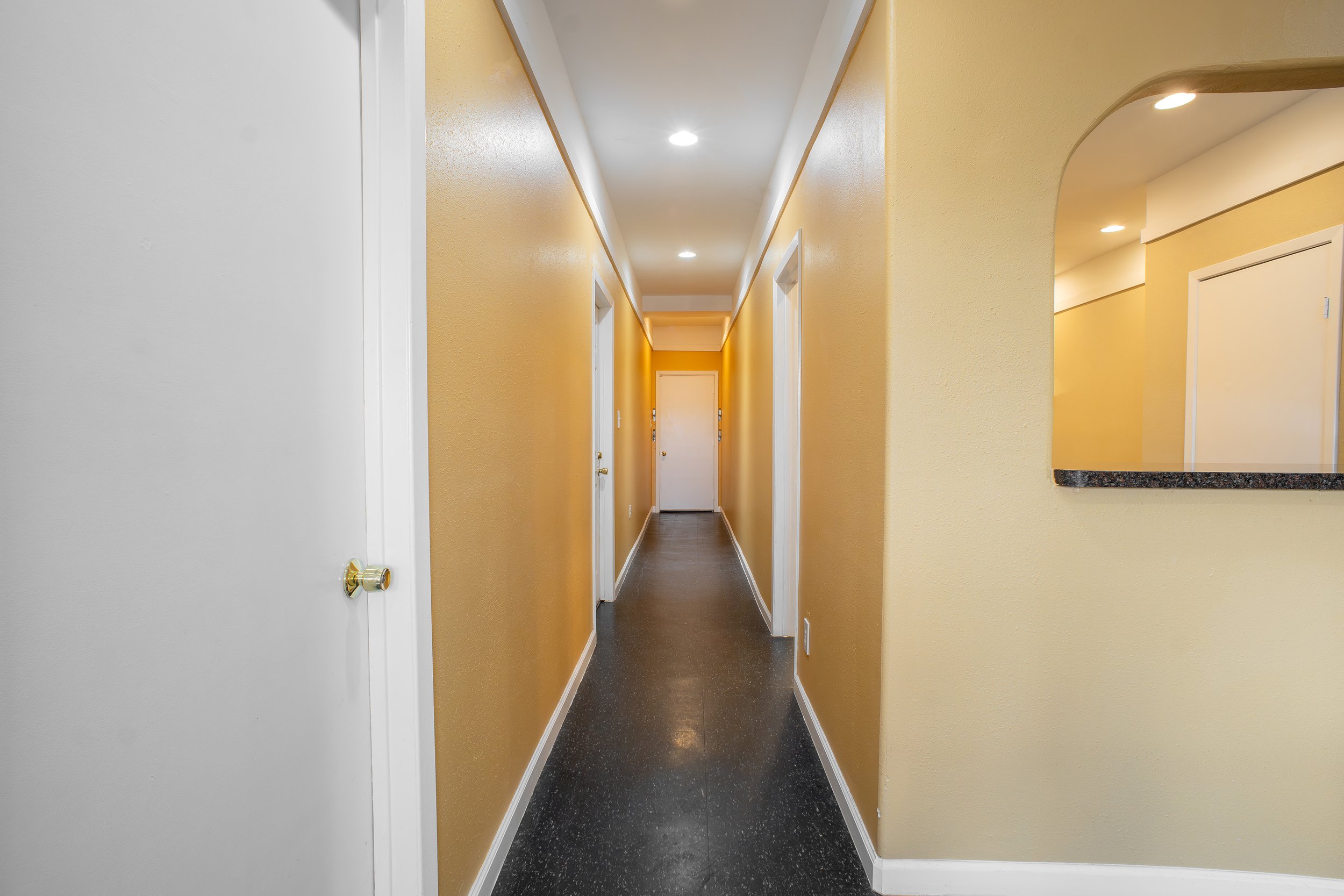 Interior hallway with yellow walls, white doors, black speckled flooring, and recessed ceiling lights.