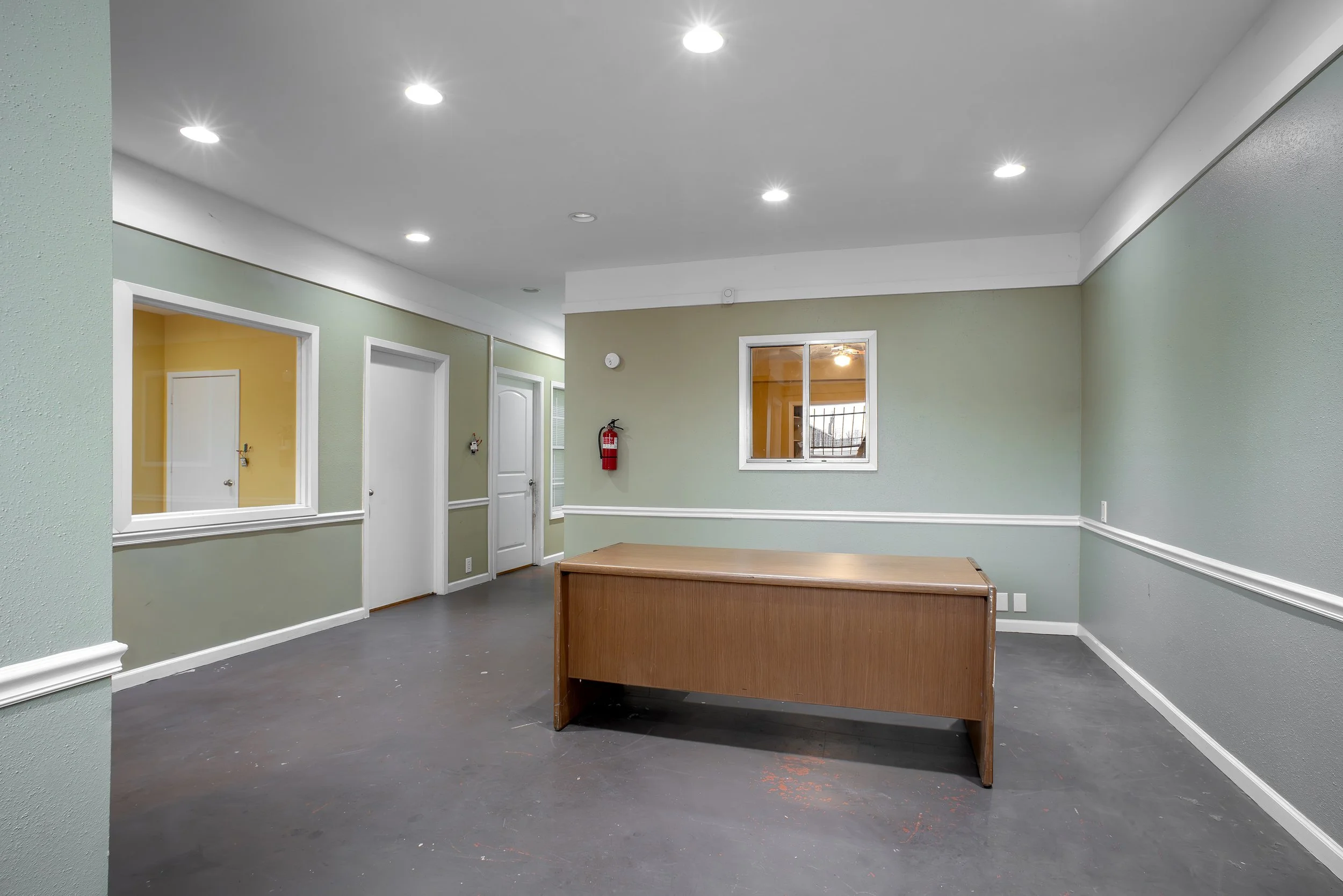 Empty room with light green walls, white trim, a small wooden table, and fluorescent ceiling lights.