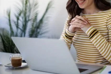 A woman in a yellow striped shirt using a laptop, with a coffee mug nearby.