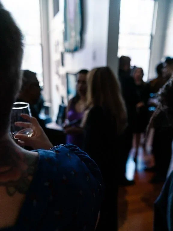 People socializing at a gathering in a dimly lit indoor space with large windows.