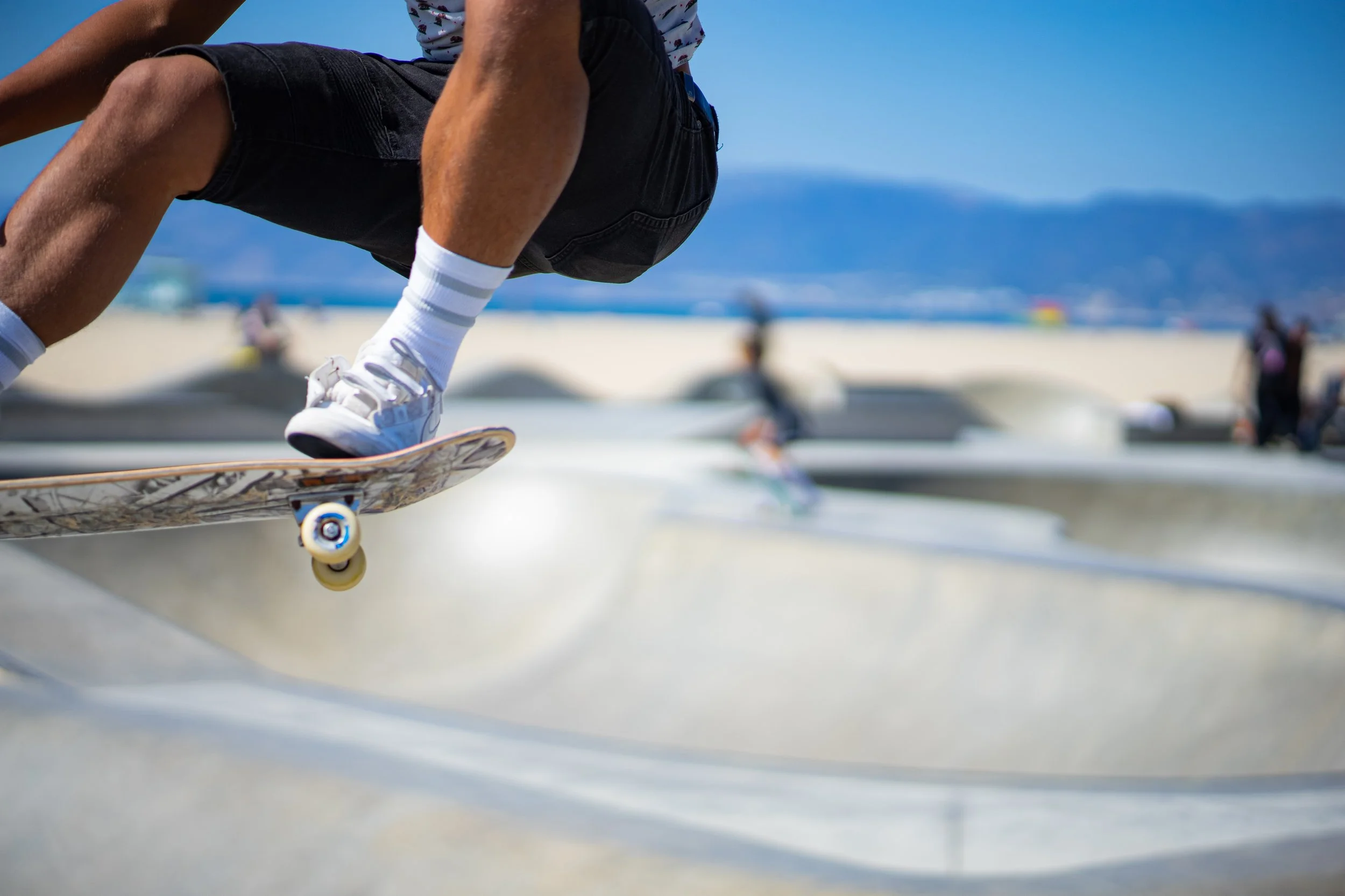 Close-up of a skateboarder executing a trick at the skate park, with other skaters and blue sky in the background.