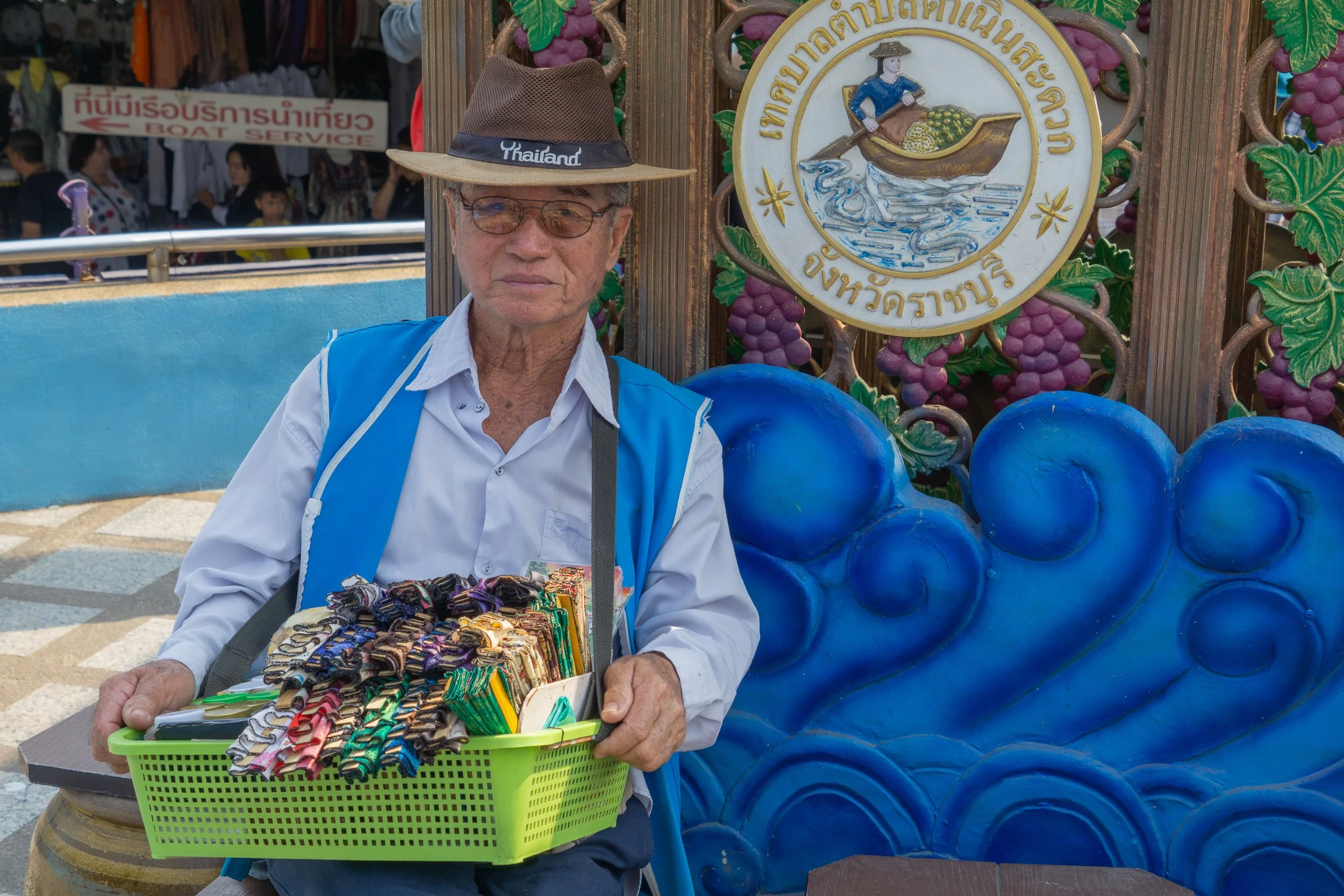 Street vendor wearing a Thailand hat selling souvenirs at a local market.