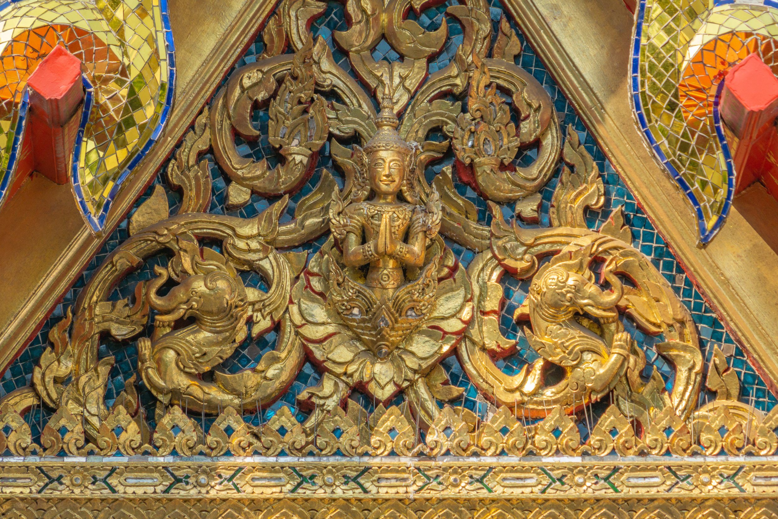 Intricate gold and blue mosaic temple pediment featuring a traditional Thai celestial figure at the Grand Palace in Bangkok.