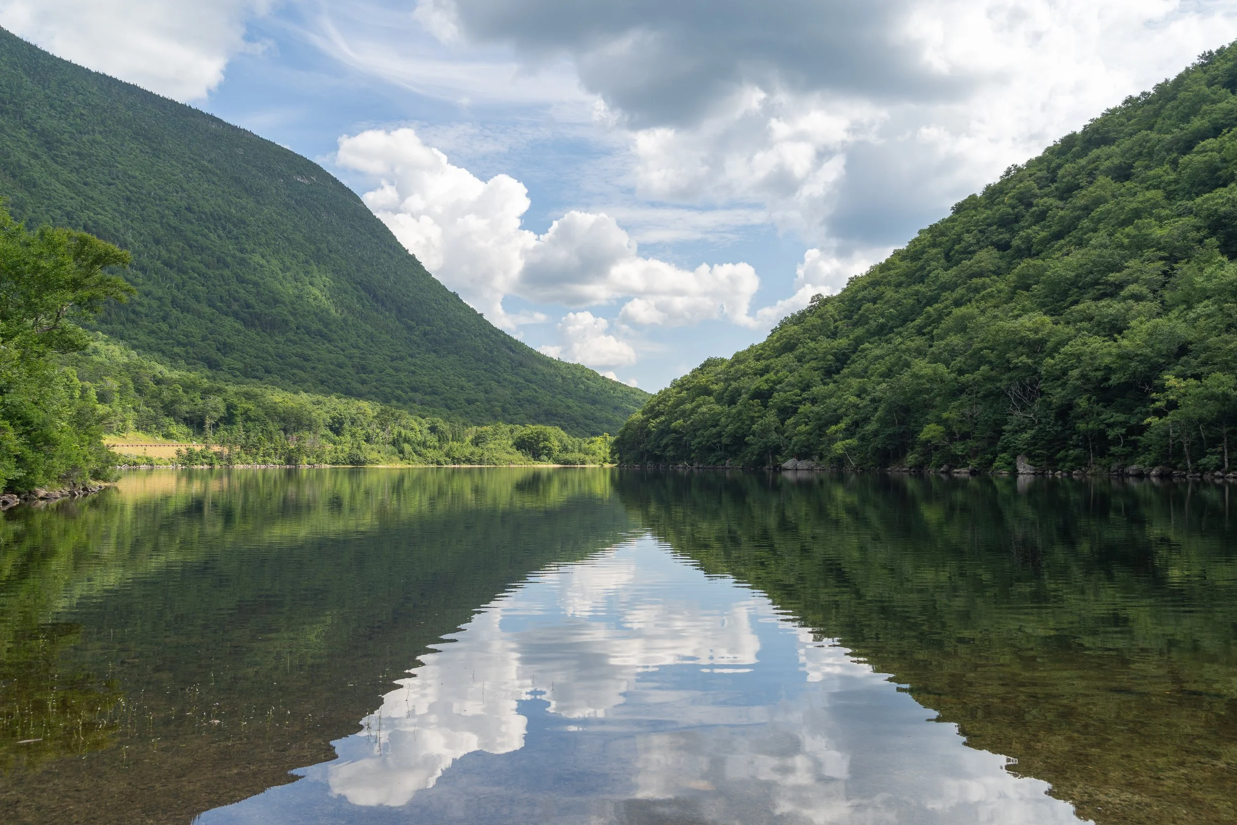 Clouds and forested mountains are reflected in the still waters of Profile Lake in Franconia Notch State Park, New Hampshire.