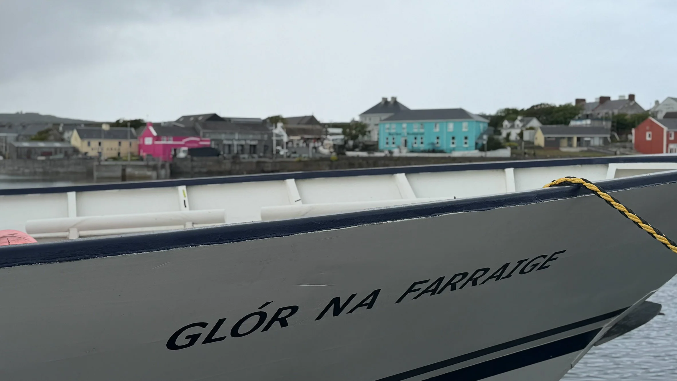 Ferry arriving at Inishmore on the Aran Islands, with colorful waterfront buildings visible beyond the bow beneath an overcast Irish sky.