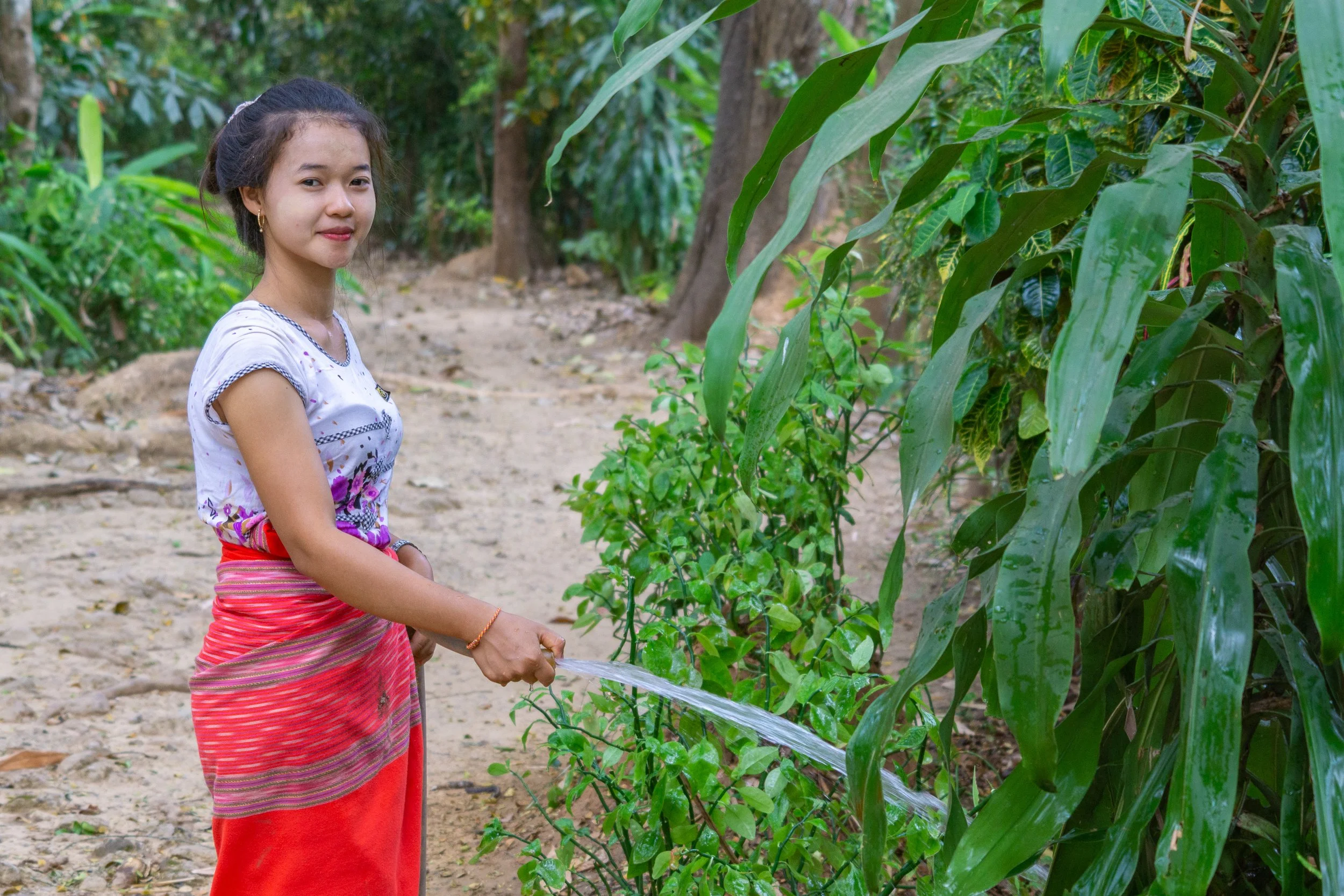 Young woman waters plants outside her home in rural Thailand.
