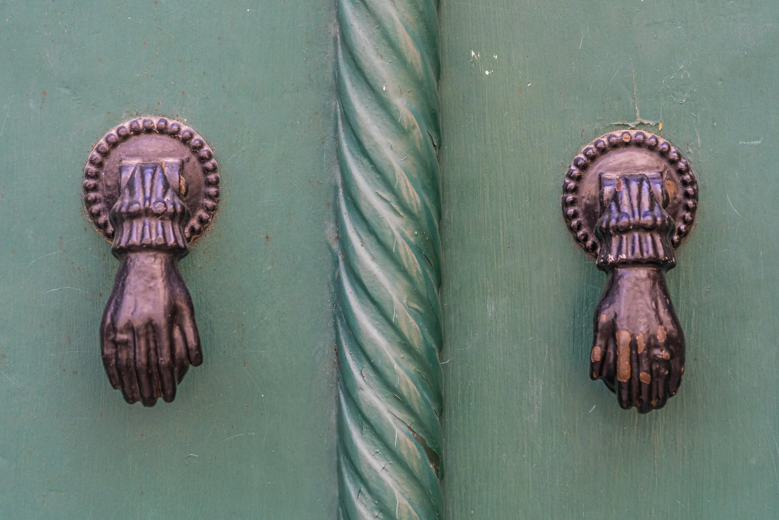 Weathered bronze hand-shaped door knockers mounted on a green wooden door in Portugal, highlighting traditional craftsmanship and architectural detail.
