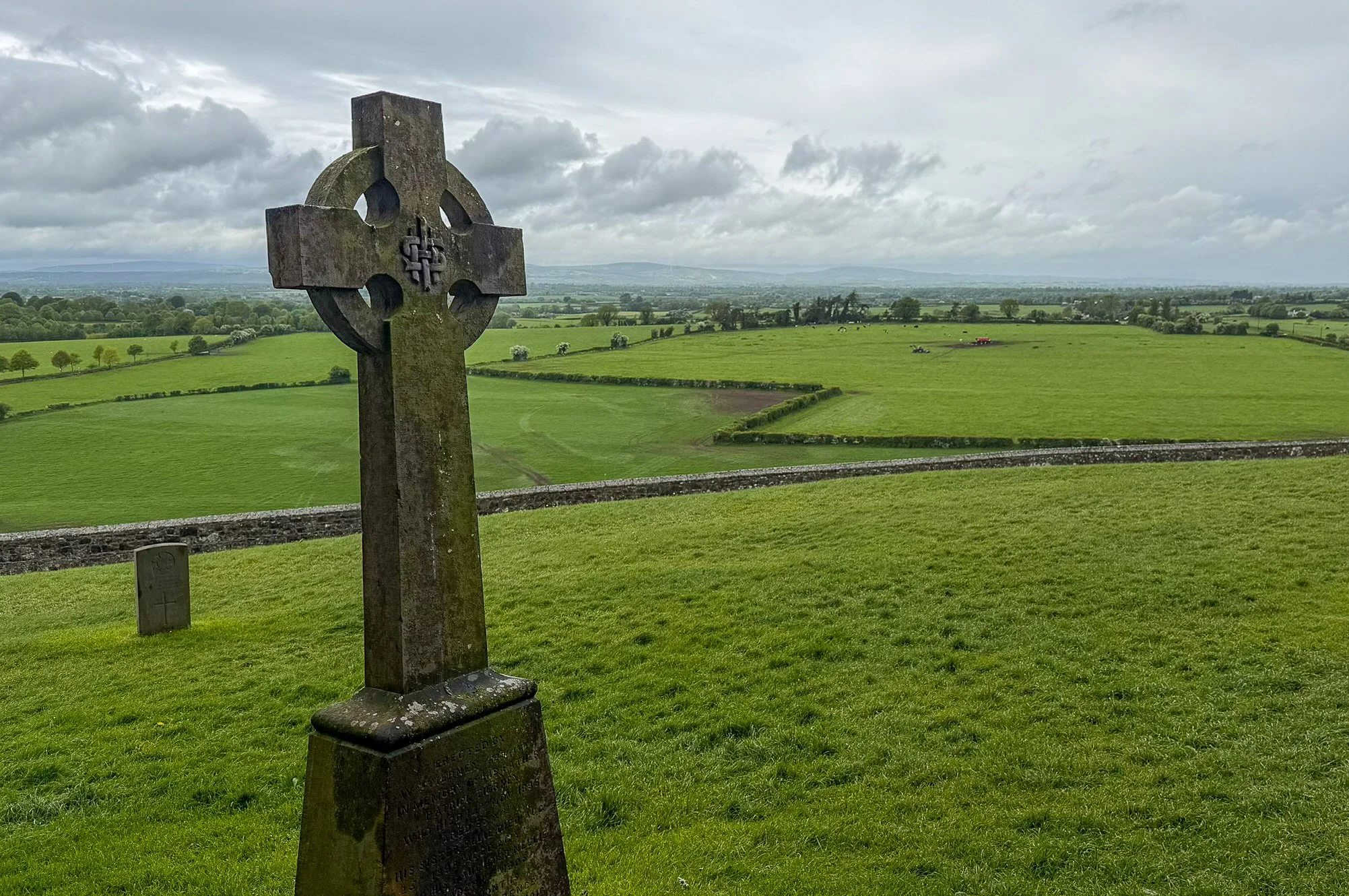 Ancient Celtic cross overlooking the green countryside from the cemetery at the Rock of Cashel in County Tipperary, Ireland, beneath dramatic spring clouds.