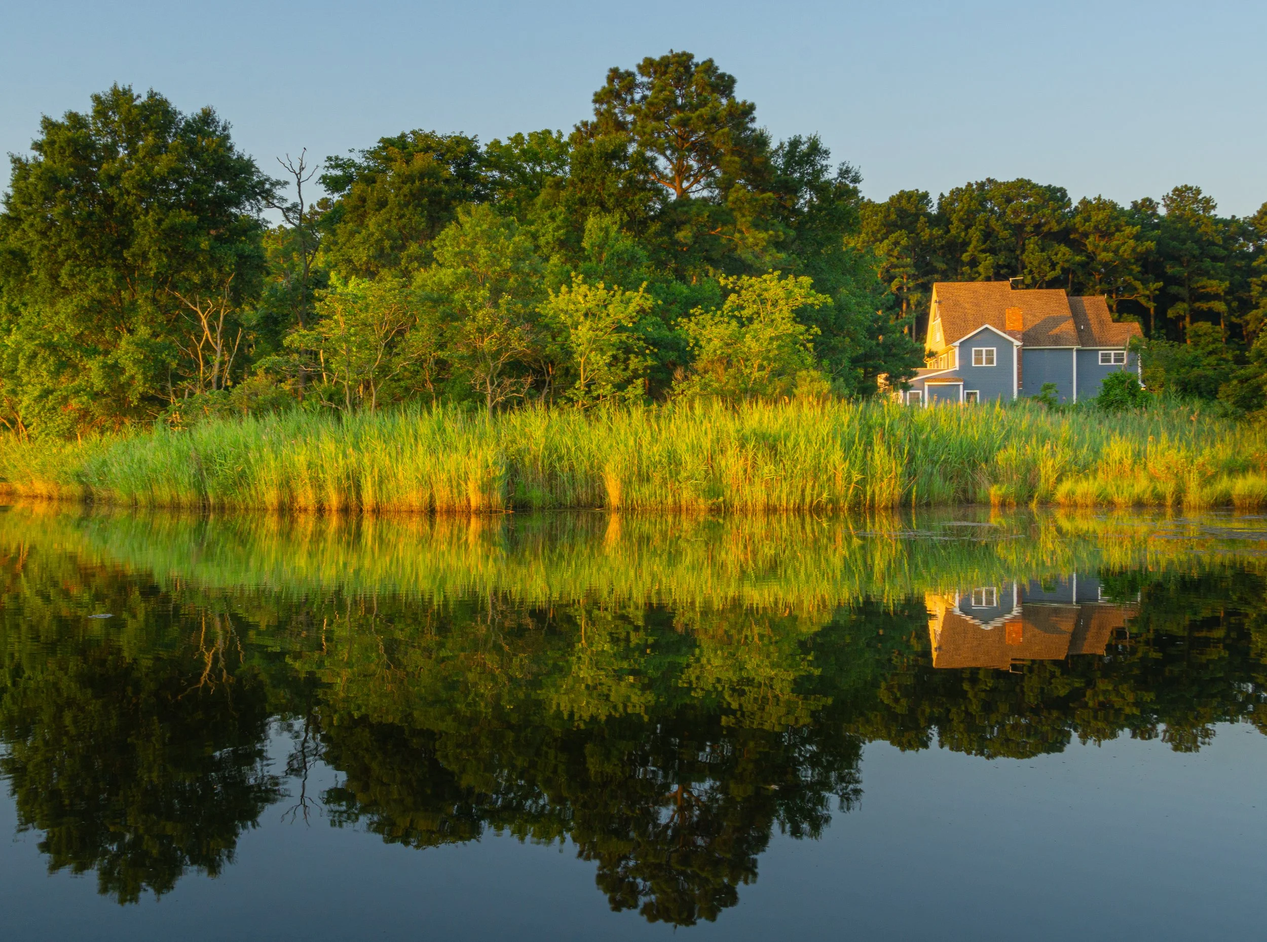 Waterfront house at Grays Inn Creek in Rock Hall, Maryland, reflected in calm water during golden hour.