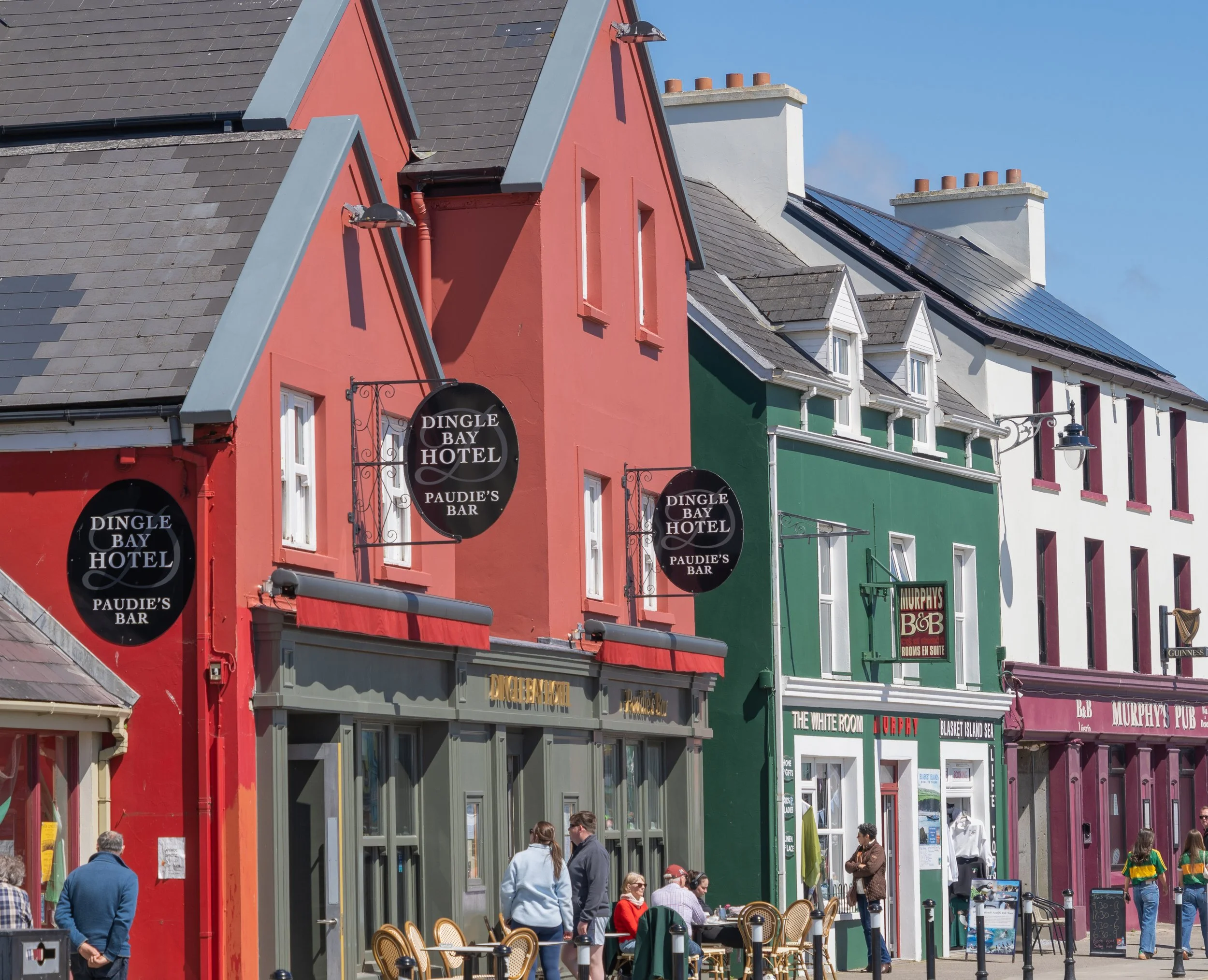 Colorful storefronts and traditional pubs along a lively street in Dingle Town, County Kerry, Ireland, on a sunny spring afternoon.