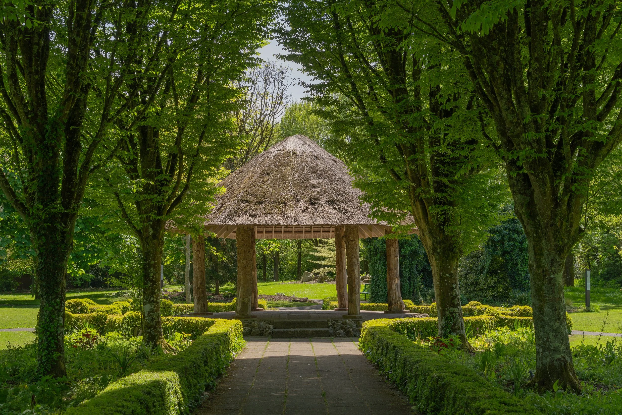 A traditional thatched gazebo framed by mature trees and manicured gardens in Adare, Ireland.