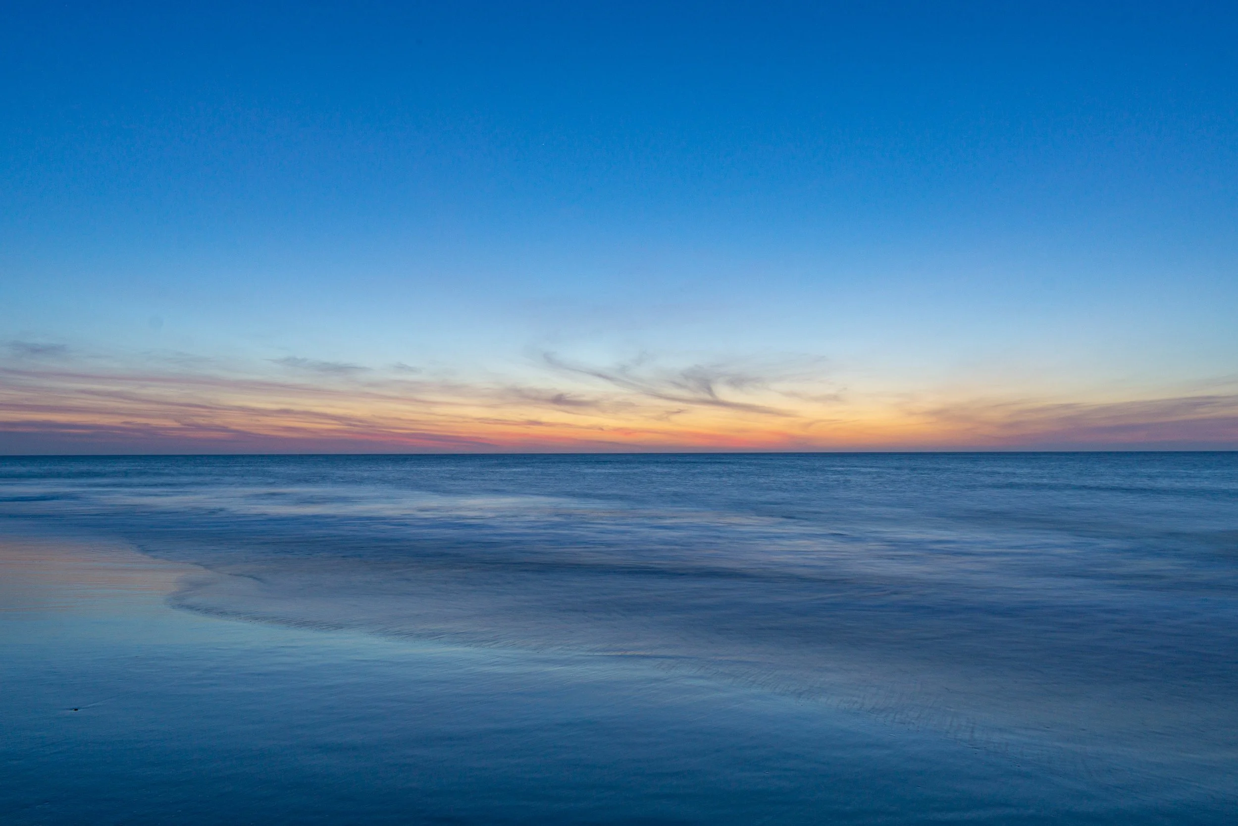 Blue-hour seascape at Rehoboth Beach, Delaware, with calm waves and a colorful sunset horizon.