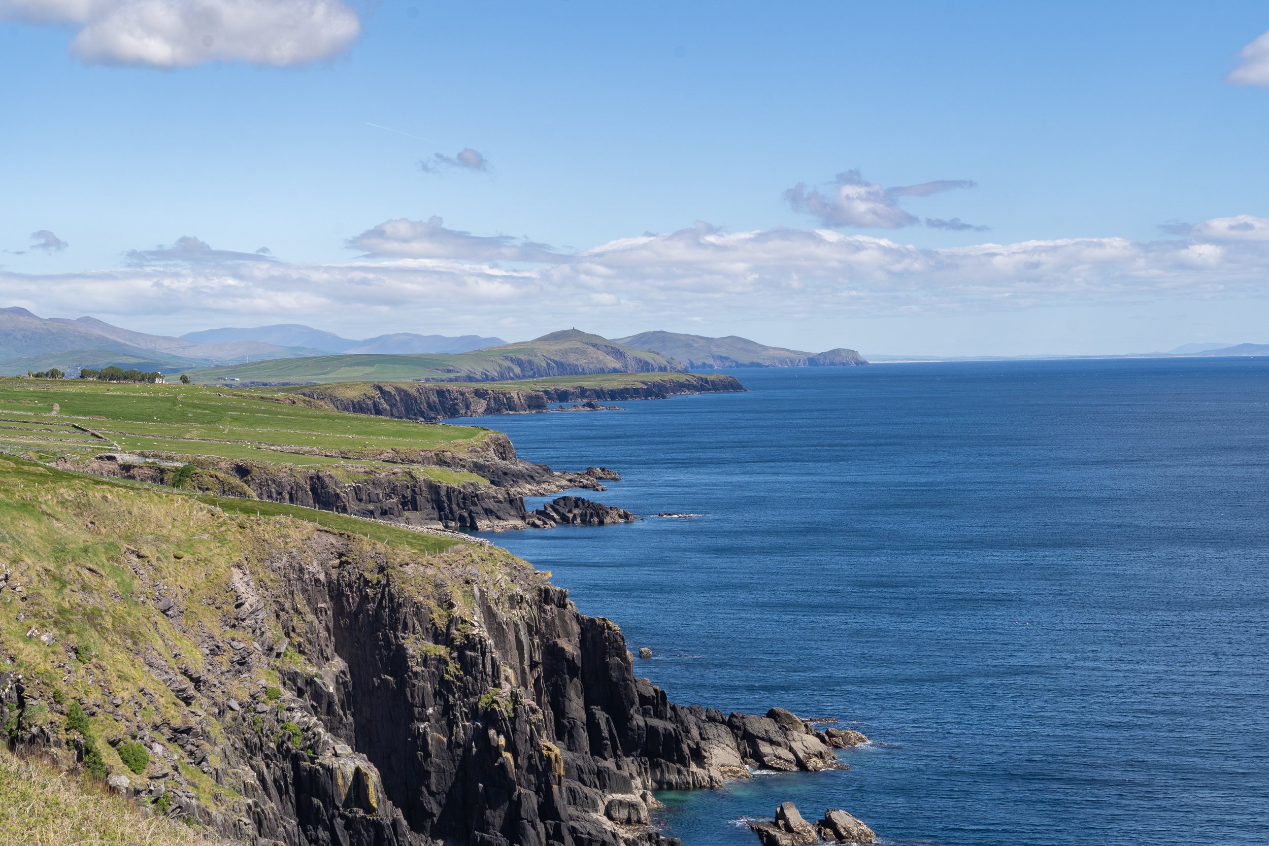 Successive rocky headlands extend into the Atlantic Ocean along the Dingle Peninsula on Ireland's Wild Atlantic Way beneath blue skies and scattered clouds.