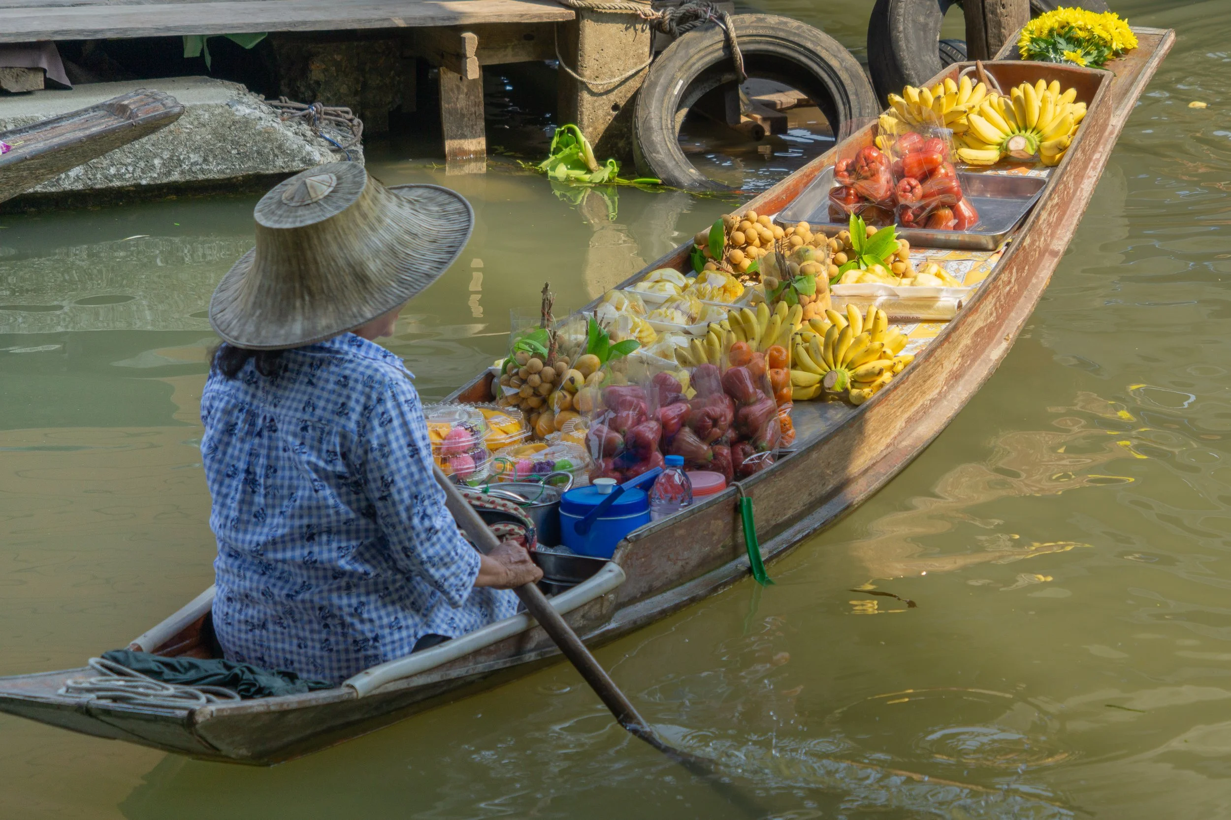 Floating market vendor paddling a wooden boat filled with fresh fruit along a canal.