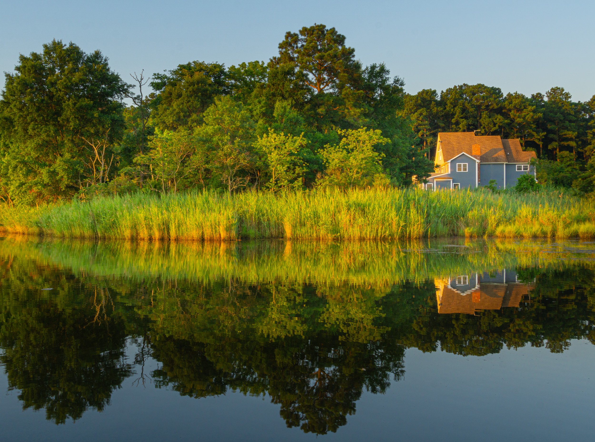 Waterfront house at Grays Inn Creek in Rock Hall, Maryland, reflected in calm water during golden hour.