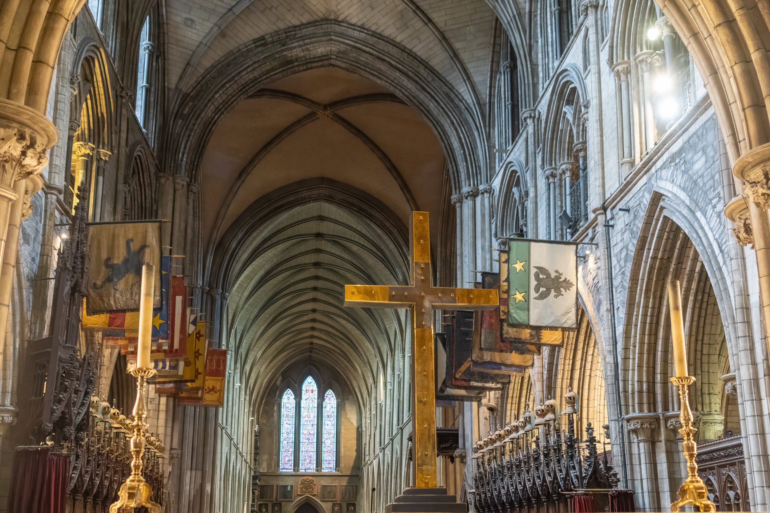 Vaulted stone arches, medieval banners, and a large golden cross inside the nave of St. Patrick's Cathedral in Dublin, Ireland.