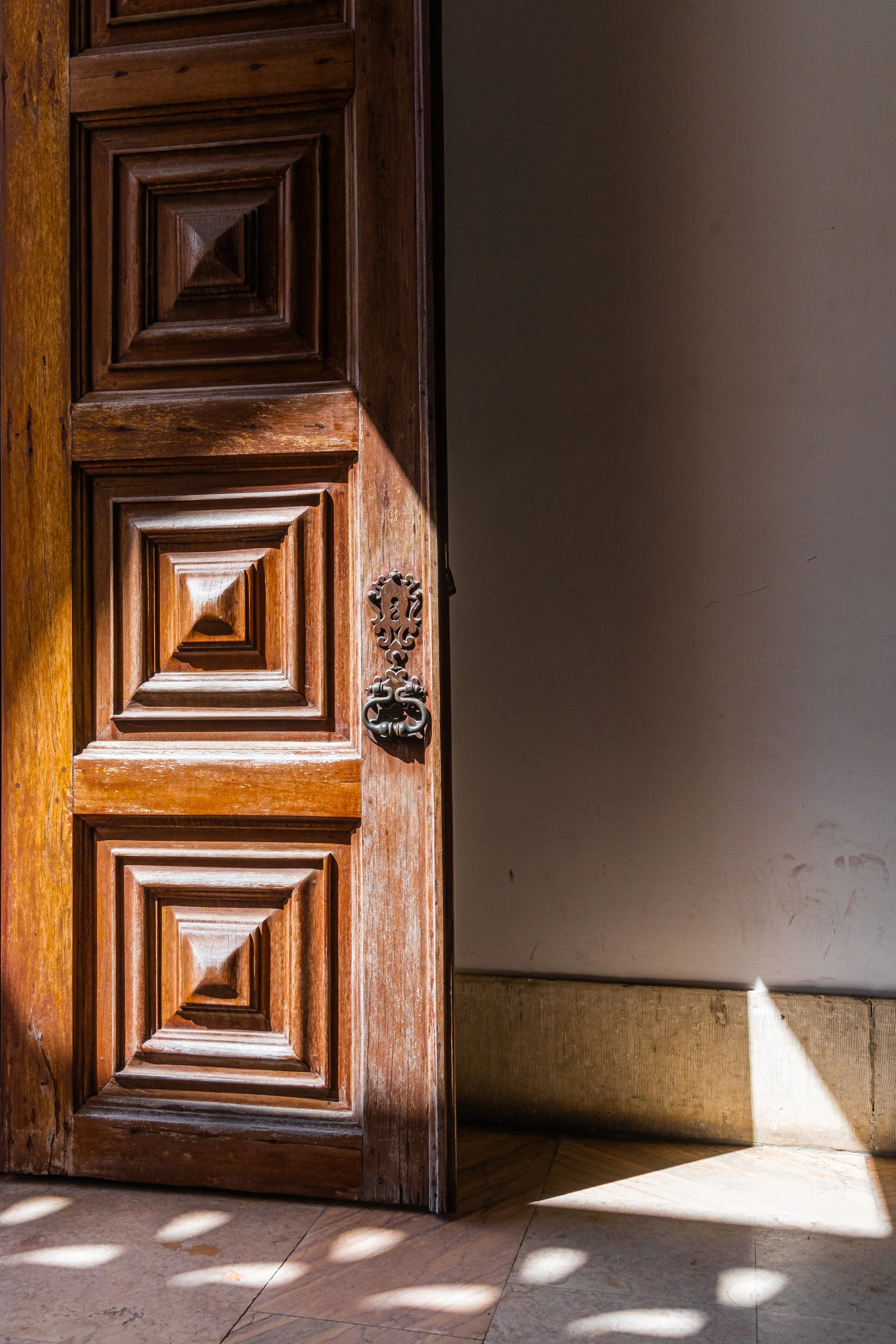 Partially open historic wooden door illuminated by warm sunlight, revealing a quiet interior in a Portuguese building.