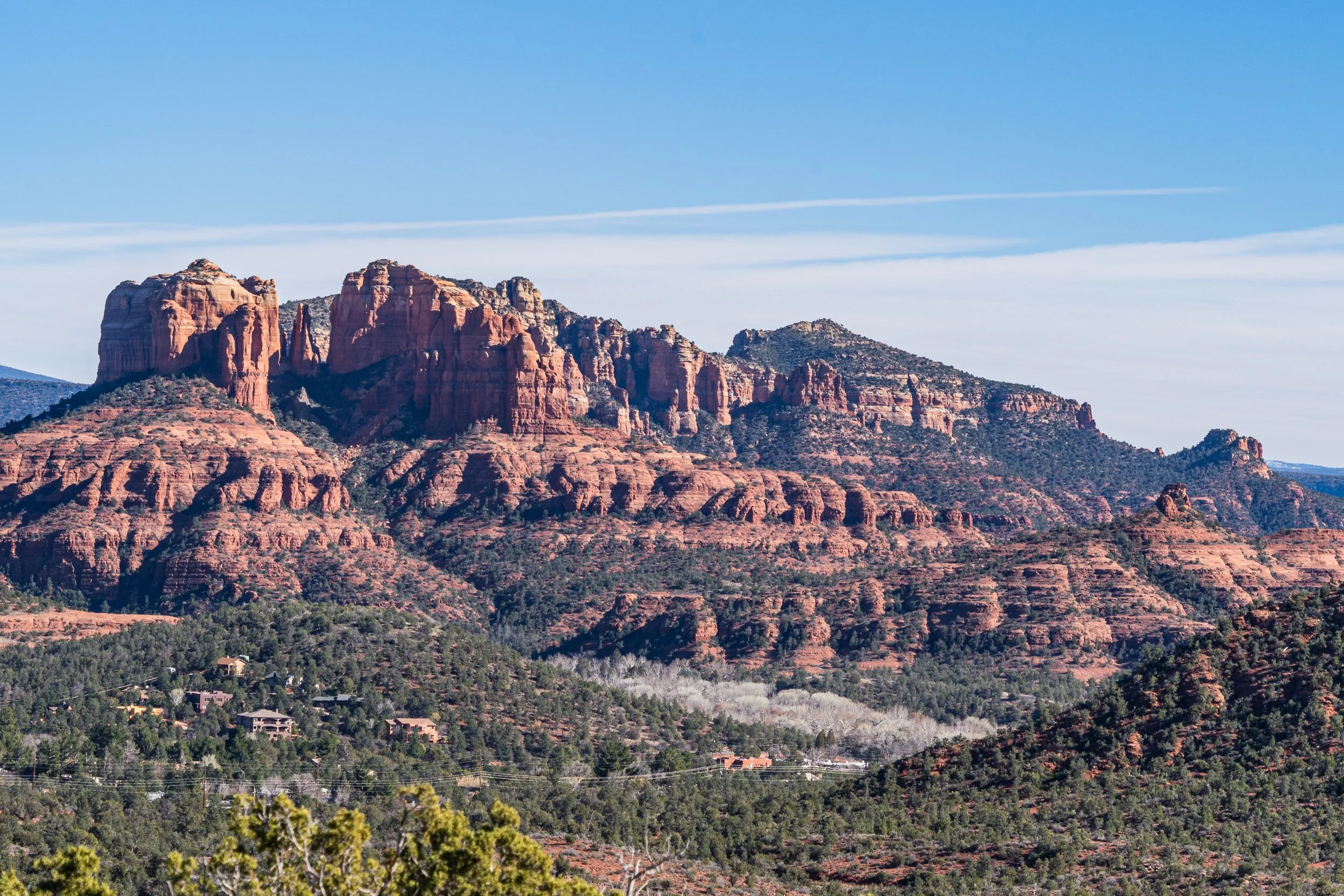 Cathedral Rock dominates the red rock landscape of Sedona, Arizona, with layered sandstone formations rising above juniper-covered hills beneath a clear blue desert sky.