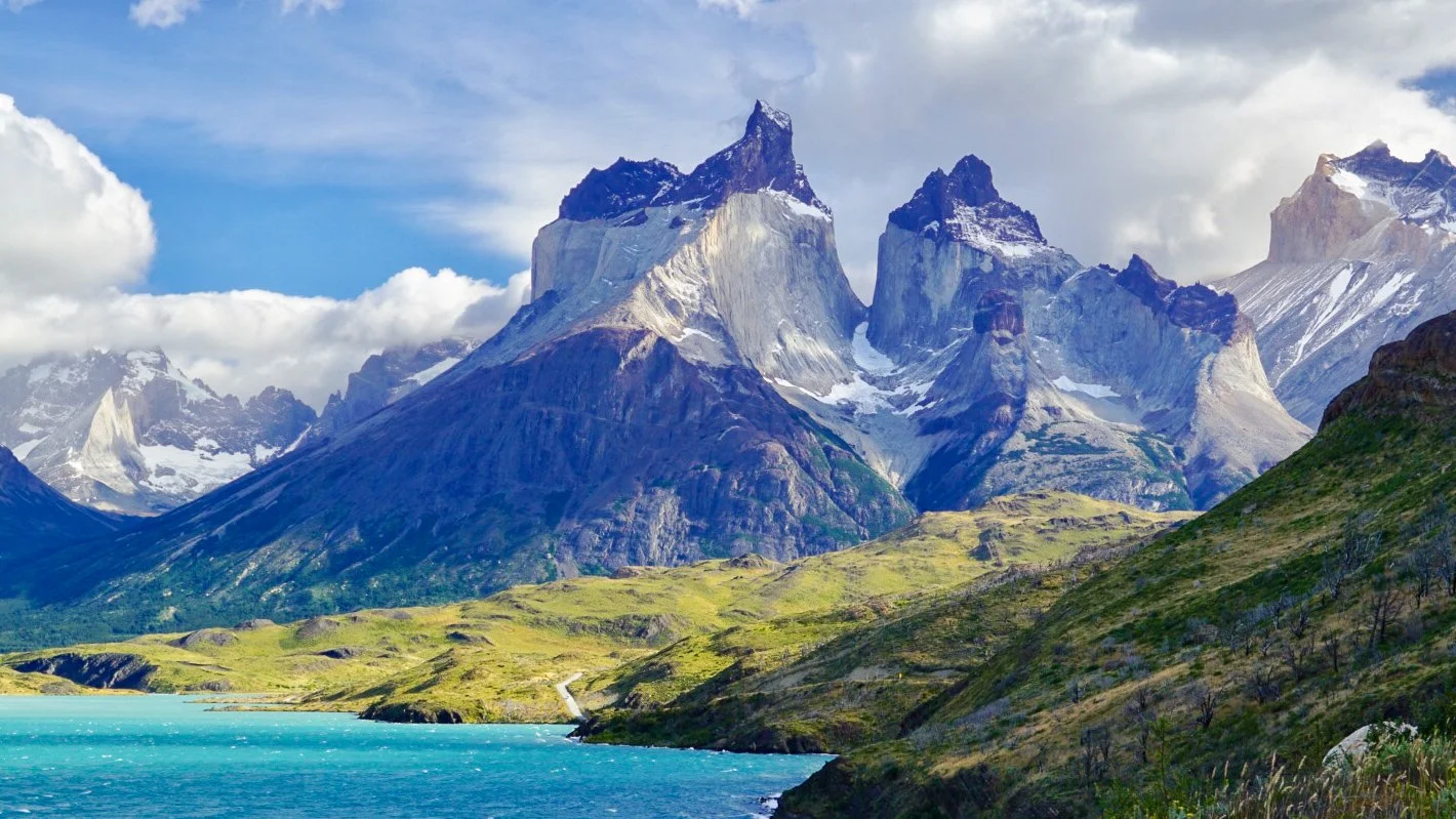 Sunlit Cuernos del Paine rise above turquoise Lake Pehoé beneath dramatic clouds in Torres del Paine National Park, Patagonia, Chile.