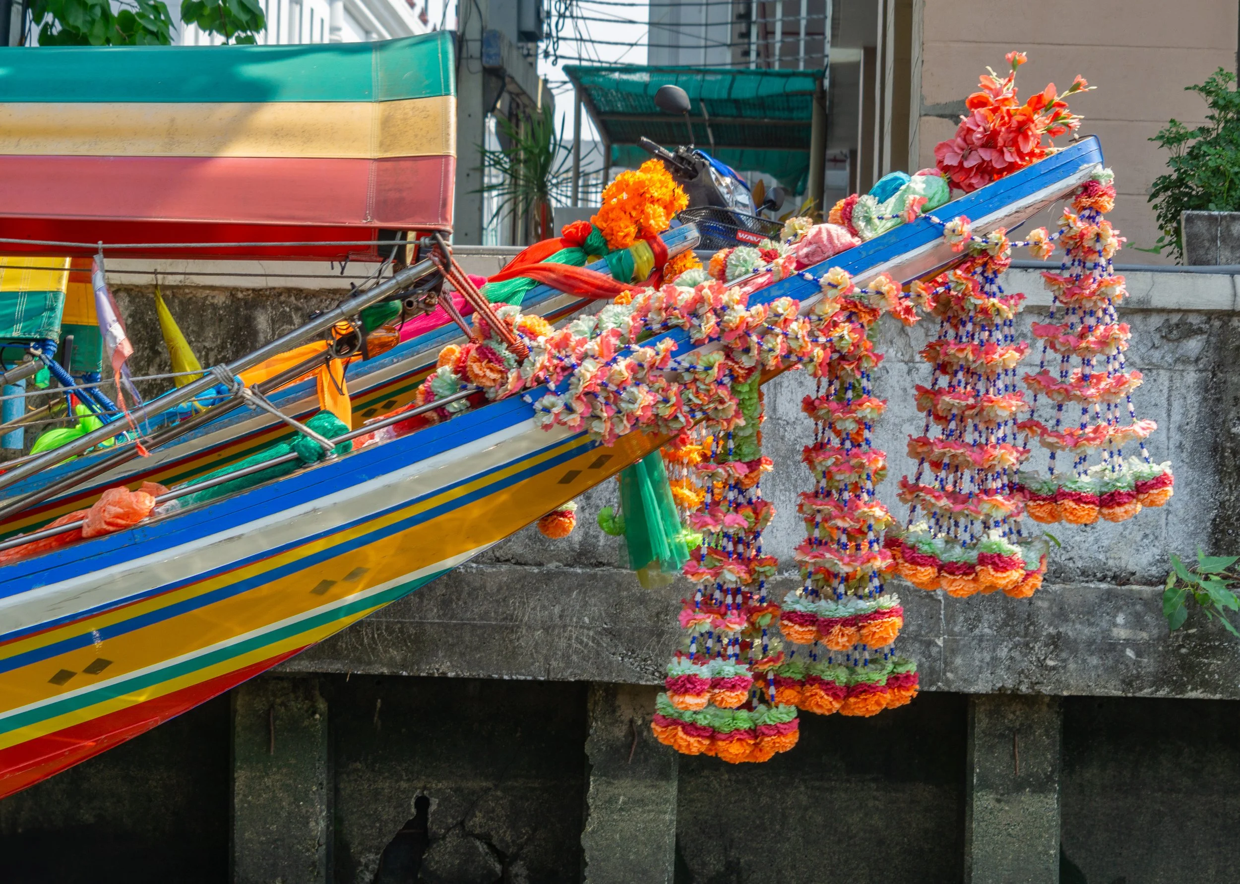 The bow of a colorful long-tail boat decorated with floral garlands along a canal in Bangkok, Thailand.