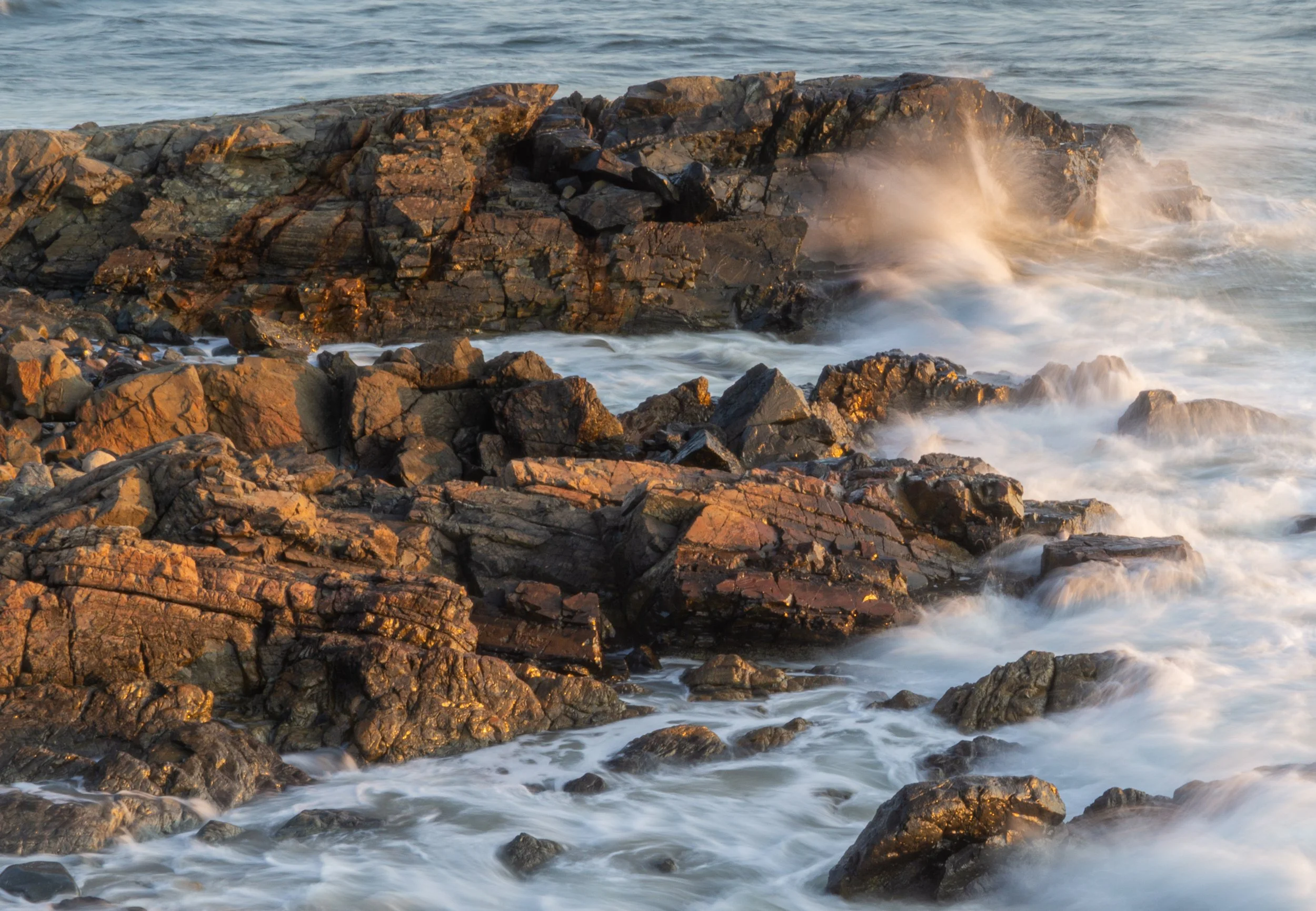 Ocean waves crashing against rocky shoreline along Marginal Way in Ogunquit, Maine, during golden hour.