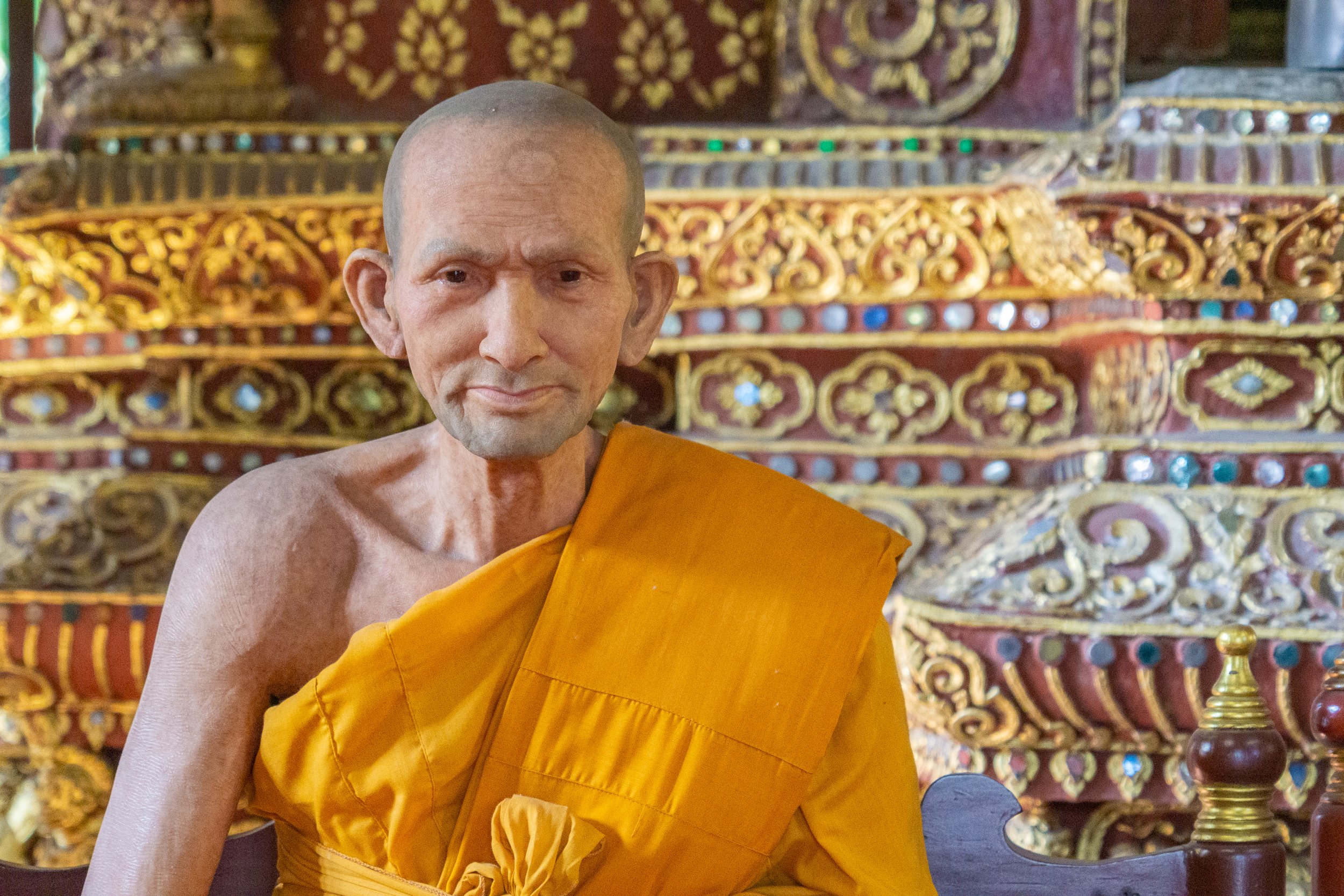 Portrait of a Buddhist monk seated inside an ornately decorated temple in Thailand.