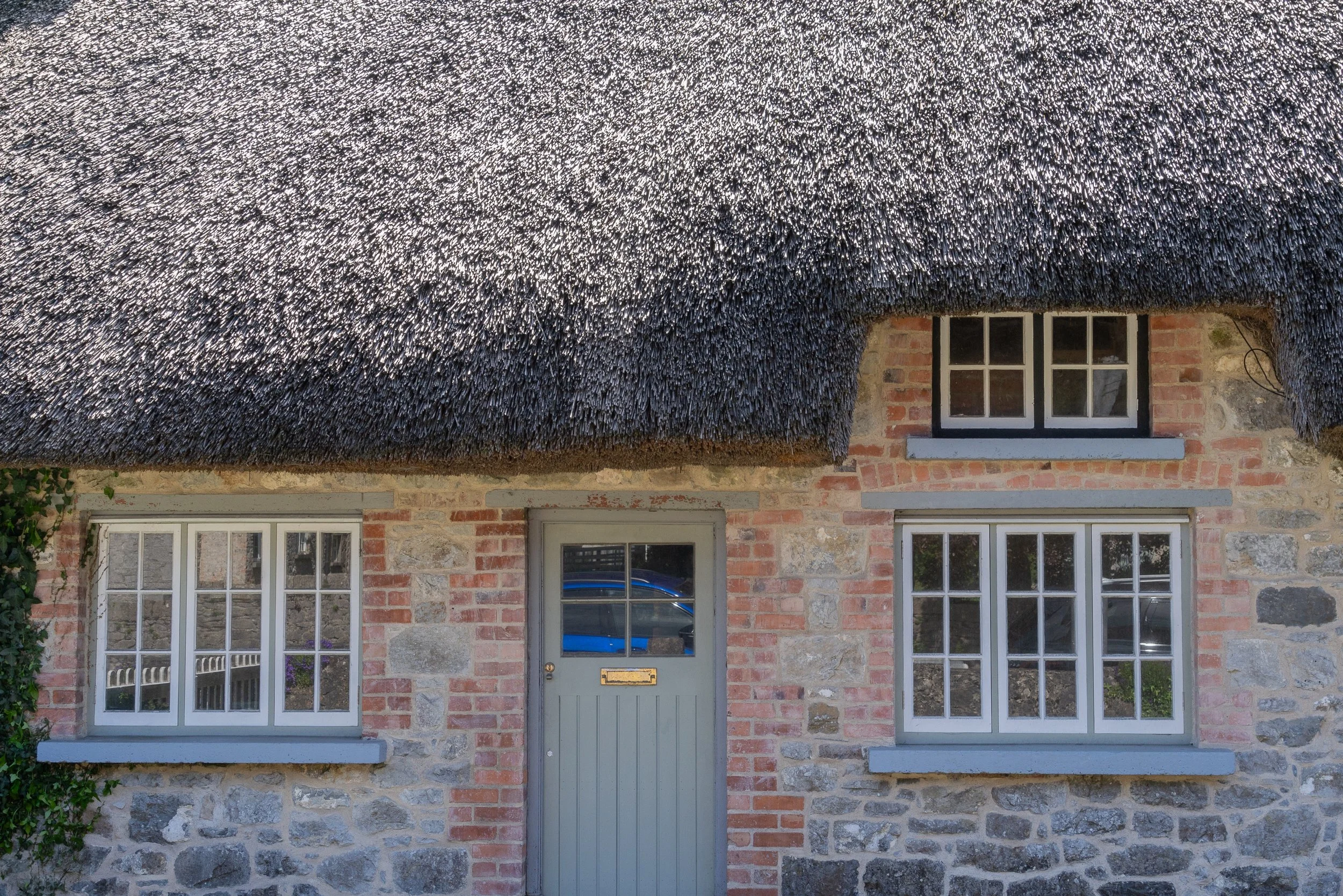 Traditional Irish stone cottage with a weathered thatched roof, sash windows, and a gray front door in Adare, Ireland.