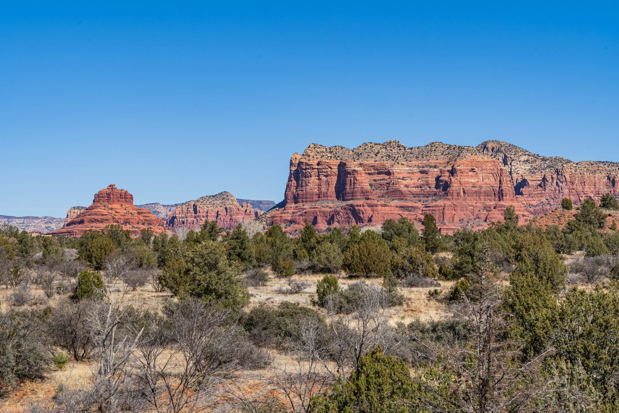 Bell Rock and Courthouse Butte rise above the juniper-covered high desert in Sedona, Arizona, beneath a brilliant blue sky.