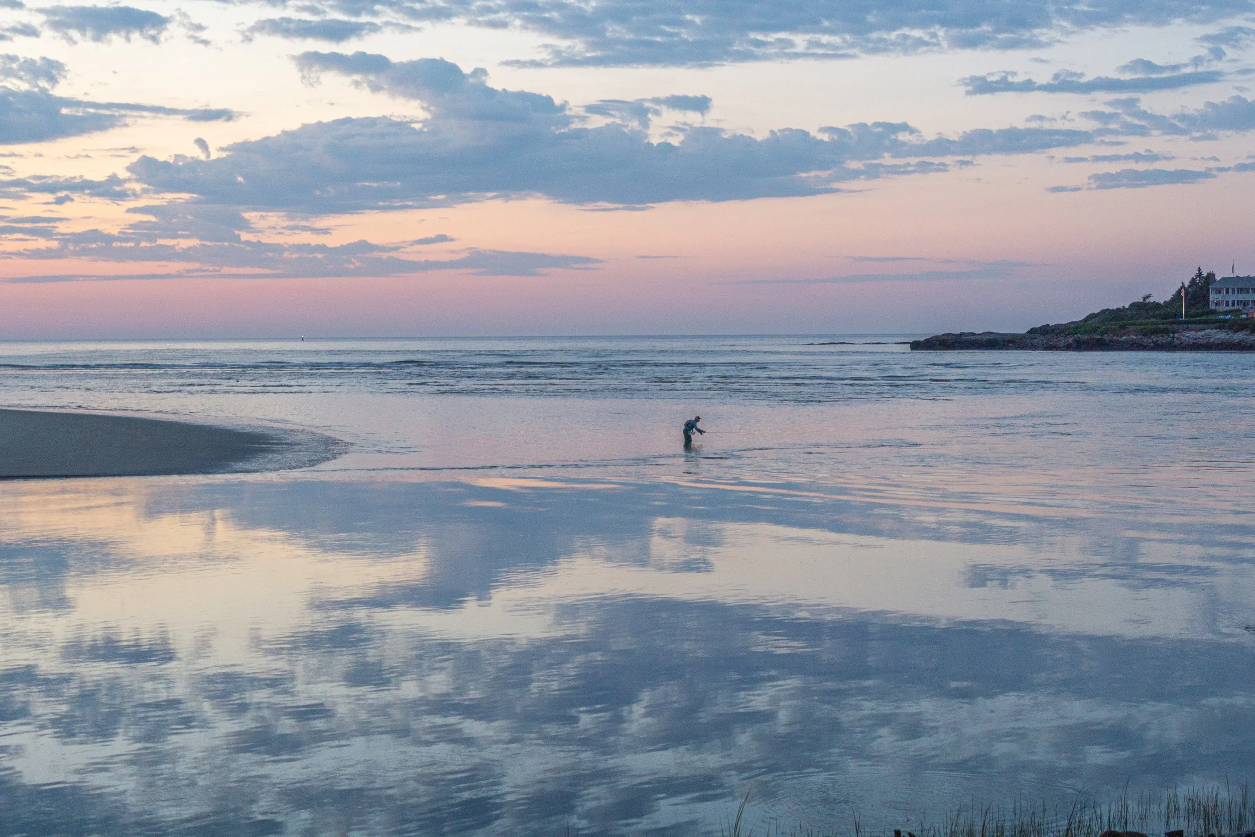 Reflections across wet sand at low tide with a lone figure walking along Ogunquit Beach