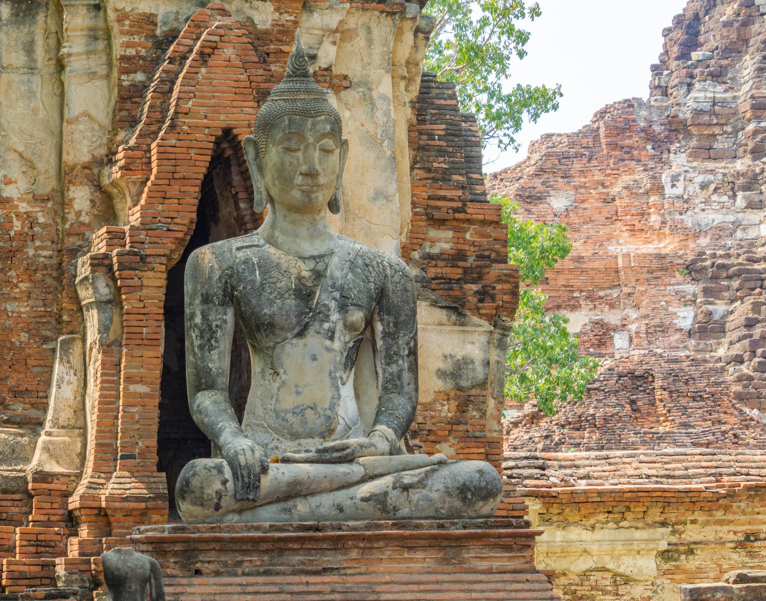 Ancient stone Buddha statue surrounded by weathered brick ruins at Ayutthaya Historical Park, Thailand.