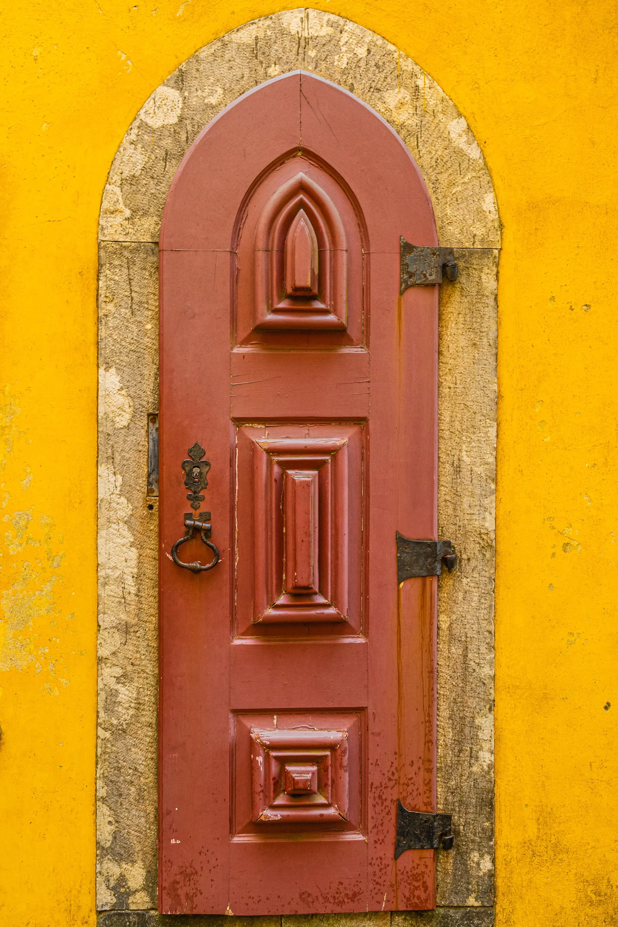Historic burgundy arched wooden doorway framed by weathered stone against a vibrant yellow wall in Portugal.