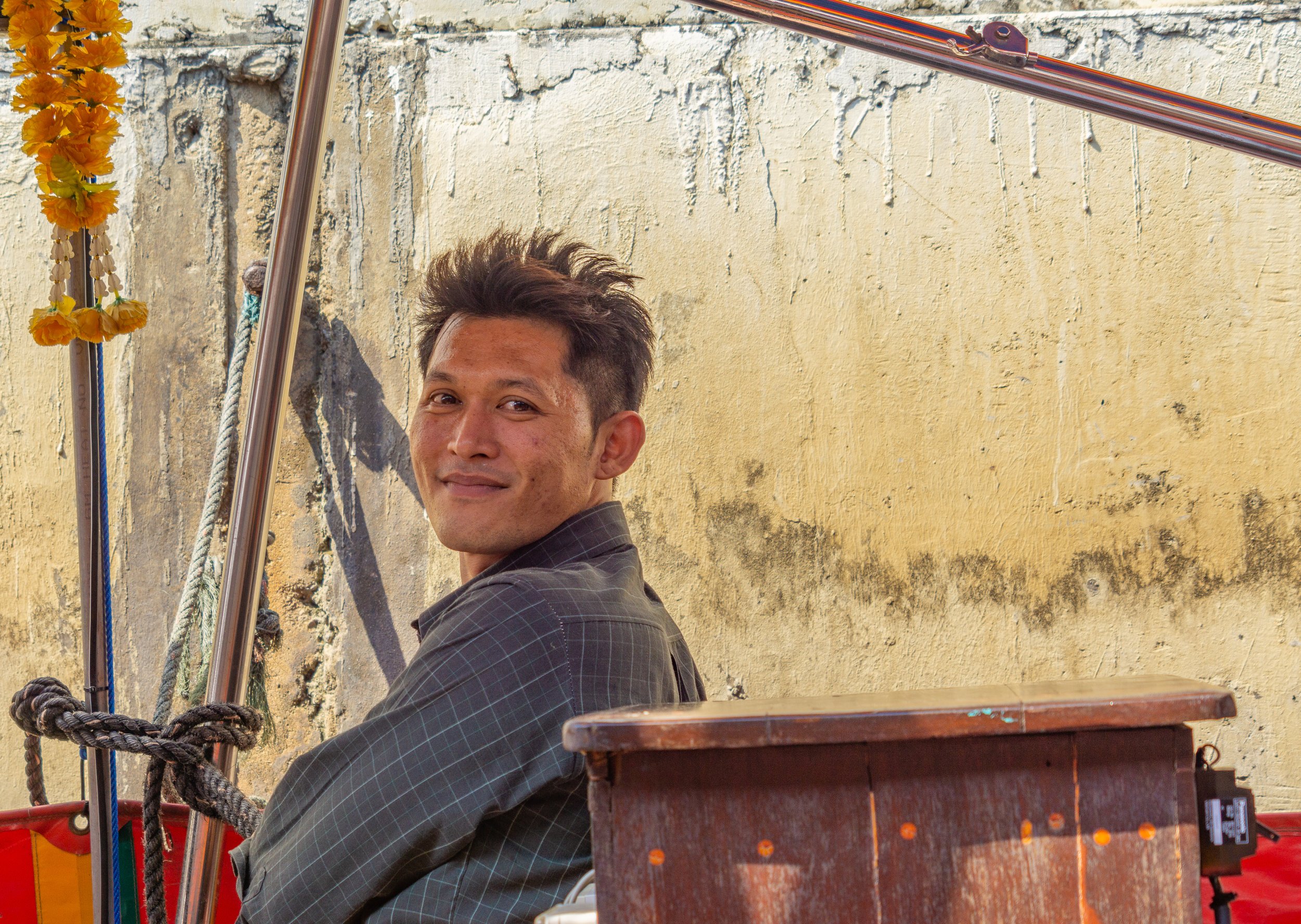 A smiling long-tail boatman glances back while preparing his boat along a canal in Bangkok, Thailand.