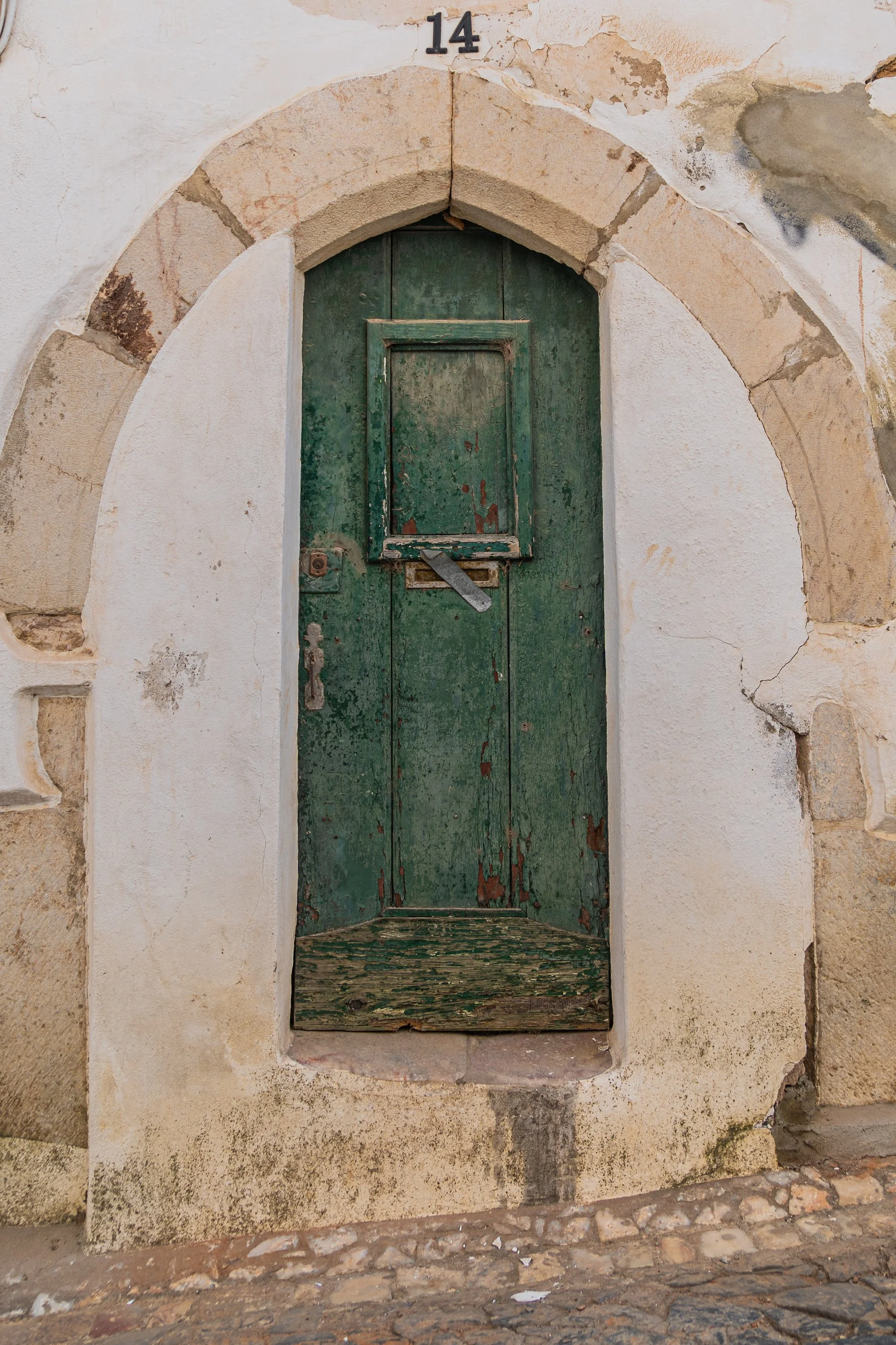 Weathered green wooden doorway set within a Gothic-style stone arch in Portugal, featuring peeling paint, worn stonework, and centuries-old architectural details.