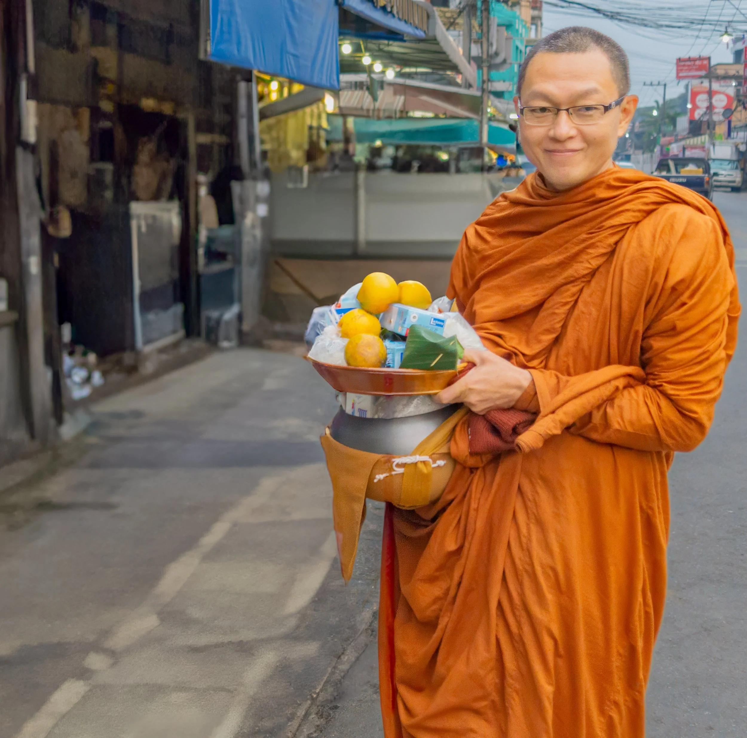 A Buddhist monk carrying his alms bowl filled with food offerings during the morning alms round on a street in Chiang Mai, Thailand.