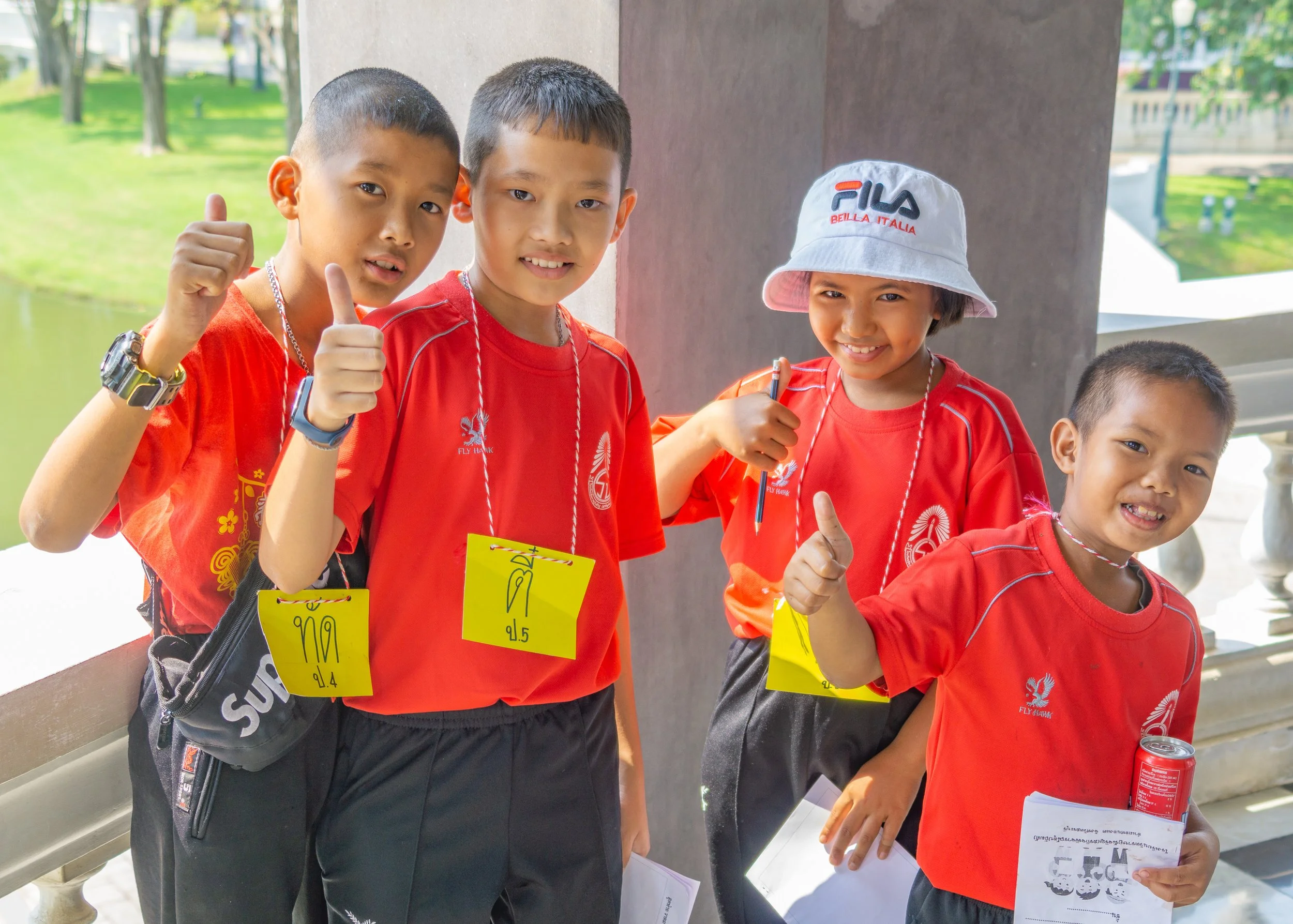 Group of smiling schoolchildren giving thumbs up while visiting a temple in Thailand.