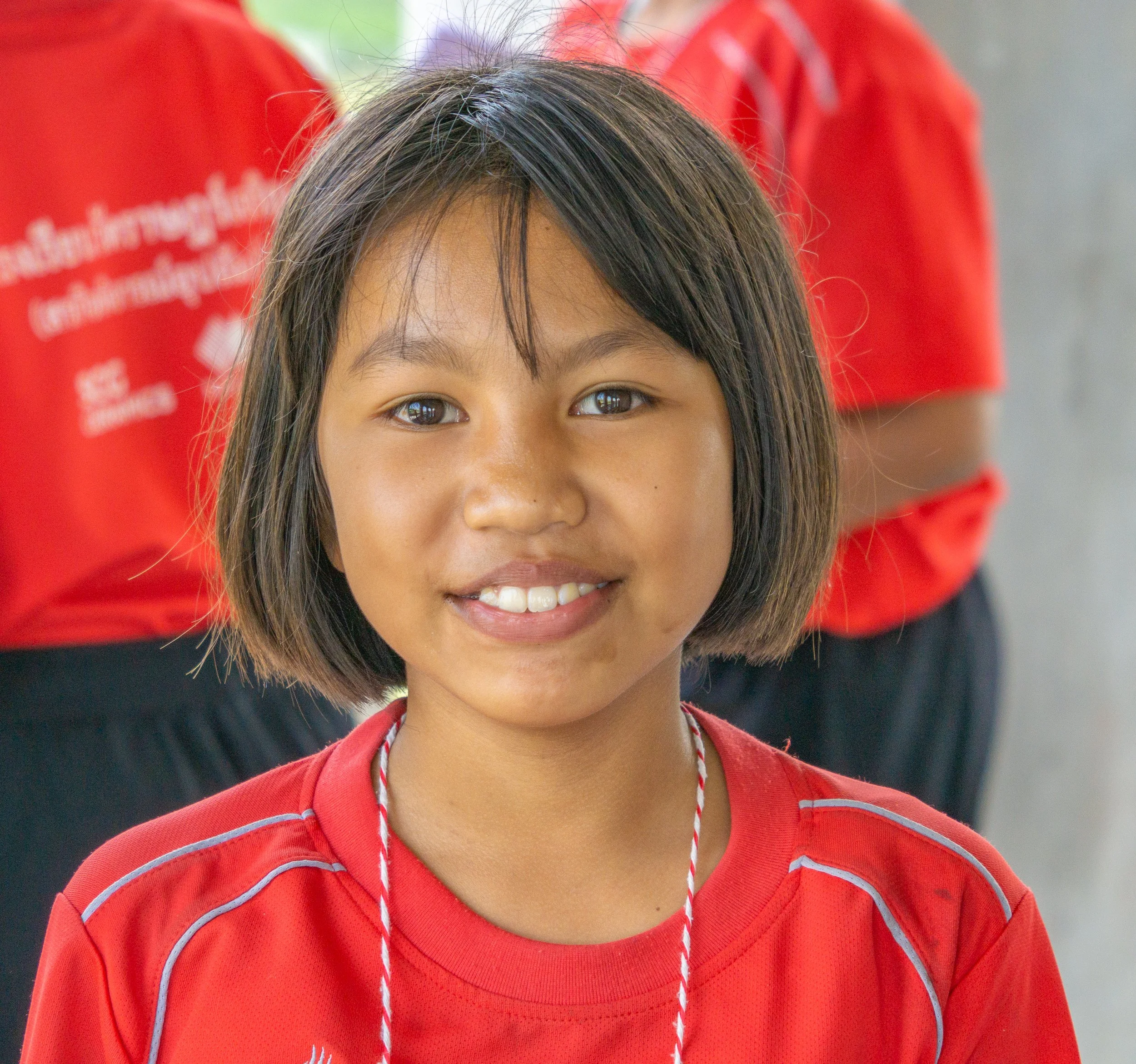 Portrait of a smiling schoolgirl wearing a red school uniform in Thailand.
